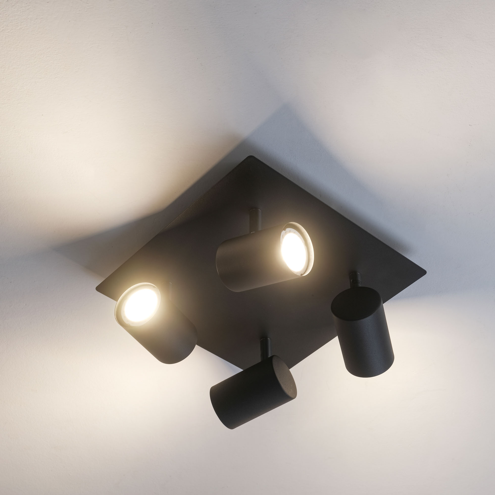 Schwarzer Deckenstrahler mit drei zylindrischen Lampen mit leuchtenden Glühbirnen. Heller Hintergrund.