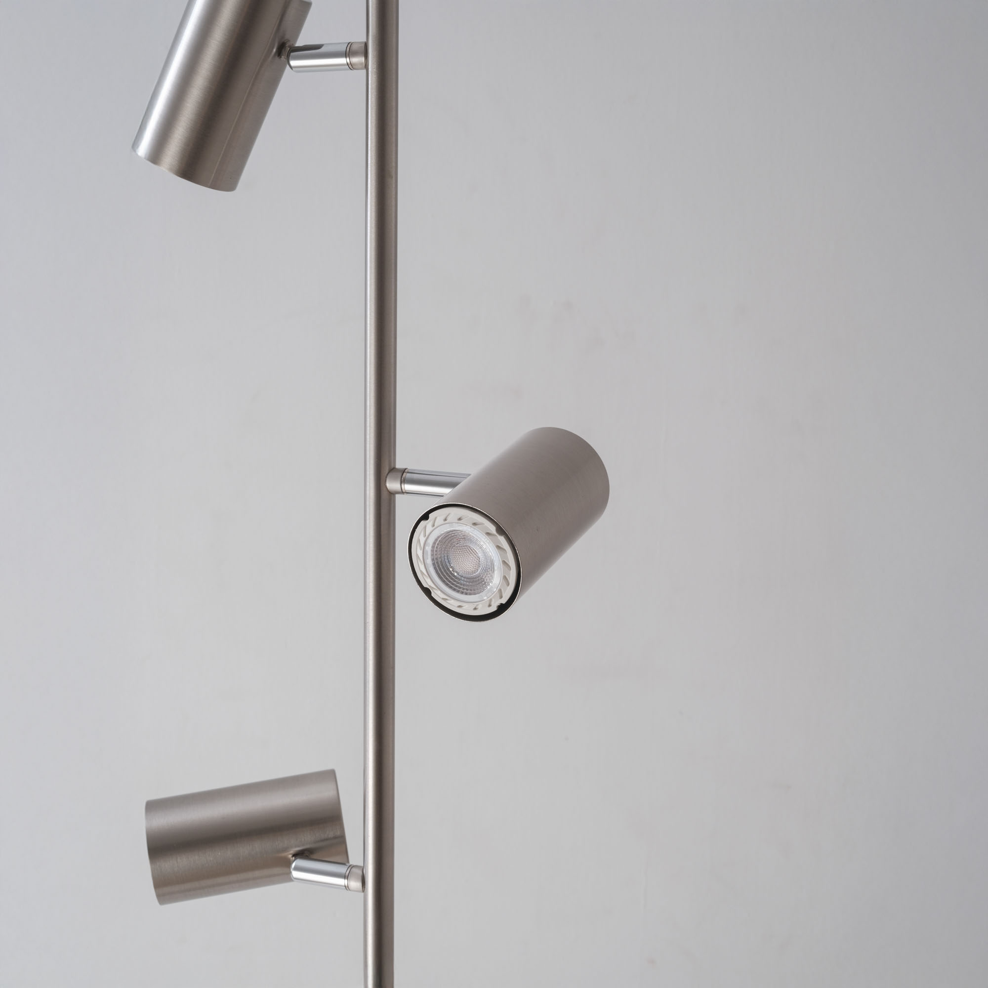 Eine silberne Stehlampe mit drei verstellbaren Strahlern vor einer weißen Wand.
