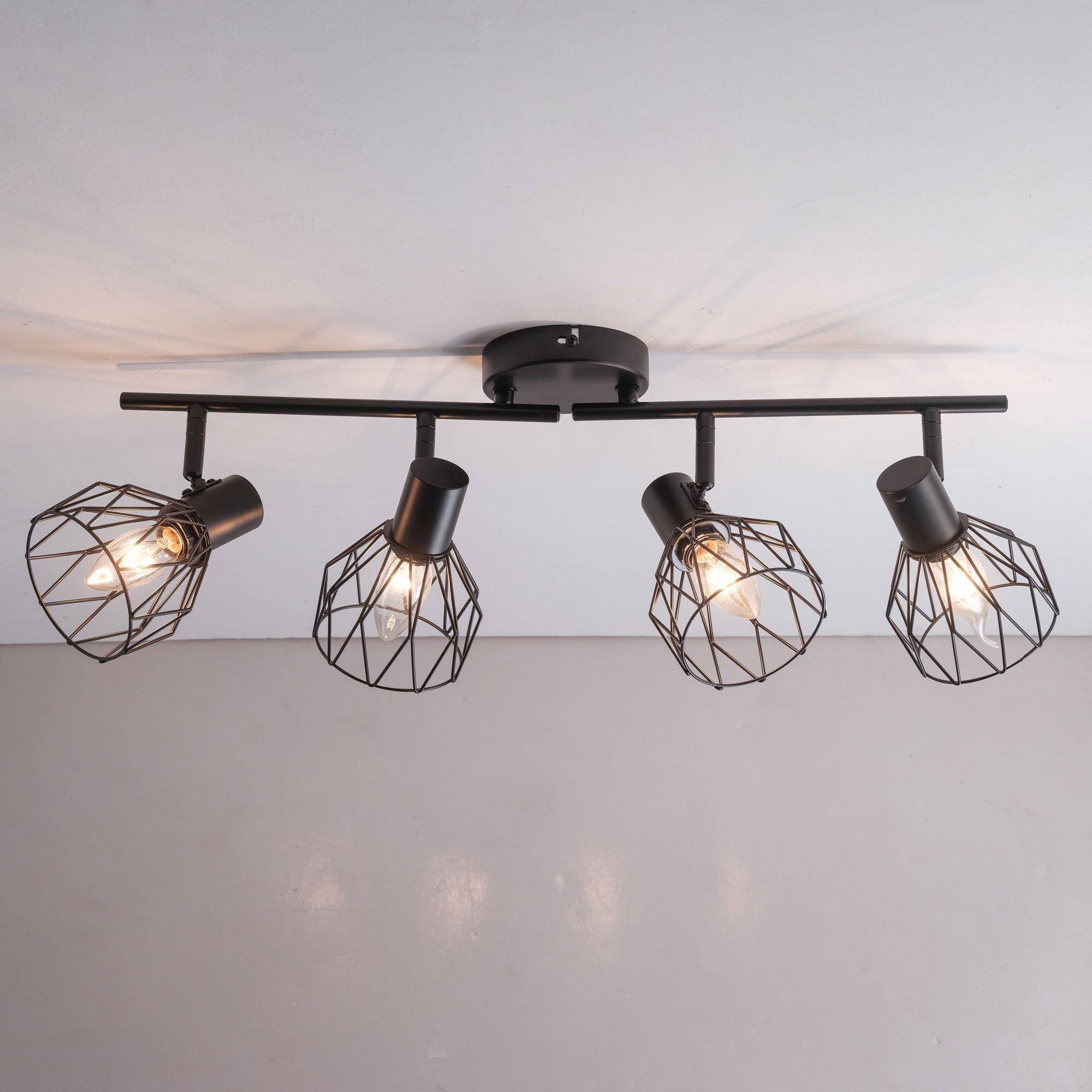 Schwarze Deckenleuchte mit vier Lampenschirmen im Käfigstil. Das Licht ist an einer weißen Decke an.