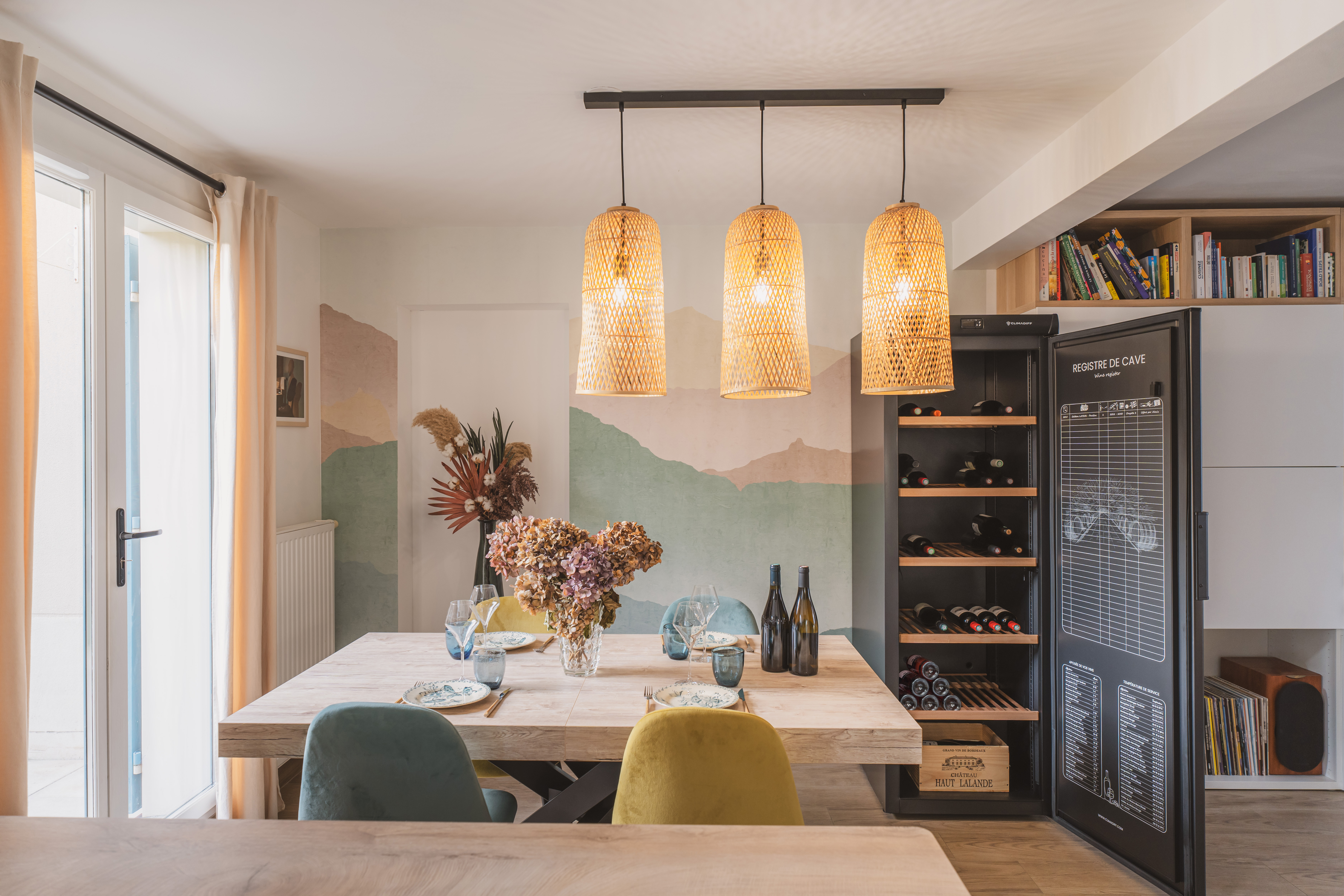 Comedor con mesa de madera, sillas, botellero y arte mural decorativo.