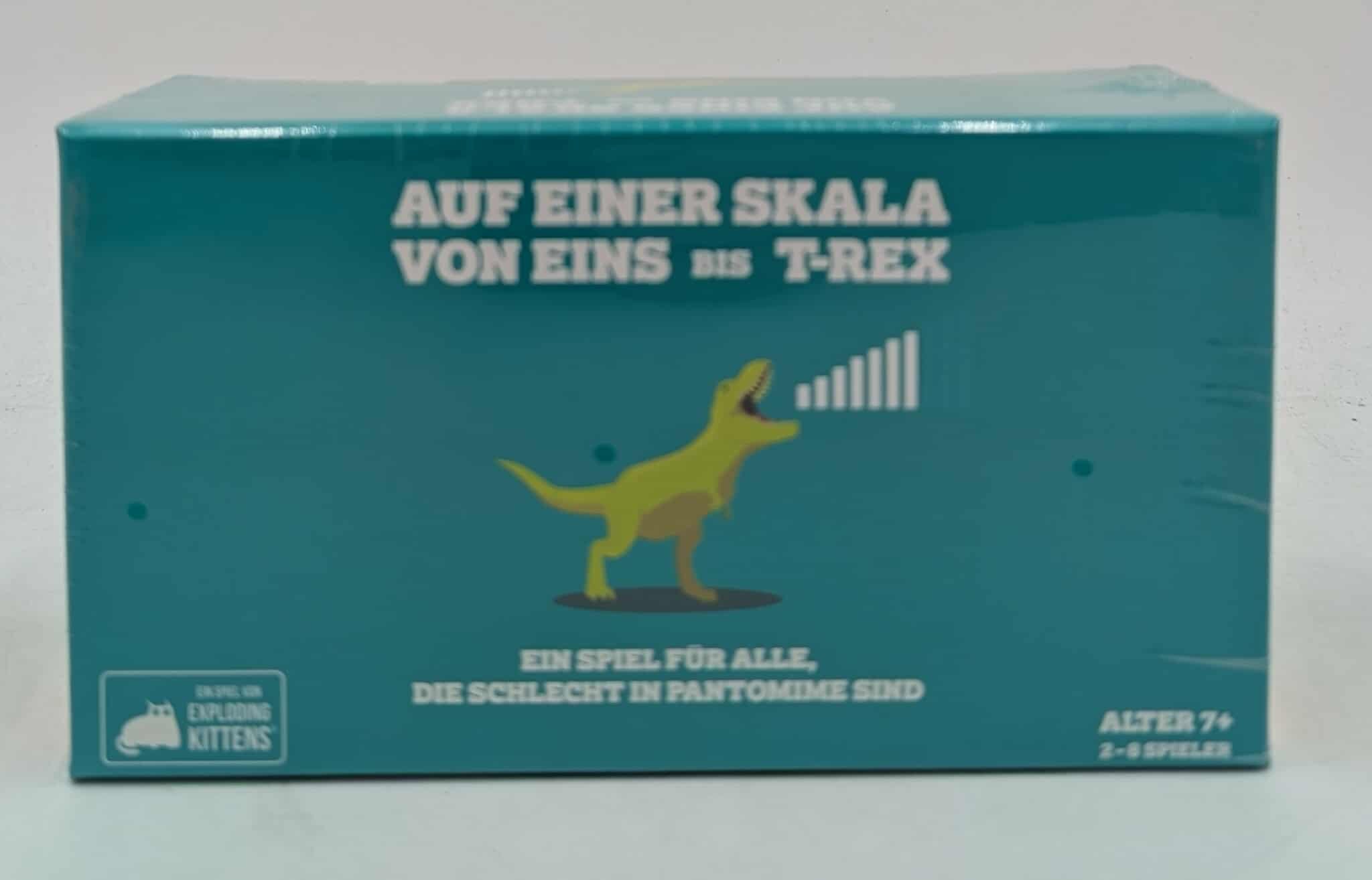 Eine türkisfarbene Box mit einem Cartoon-T-Rex, Text auf Deutsch und einem Spieletitel auf Englisch. Es ist eine Spielbox.
