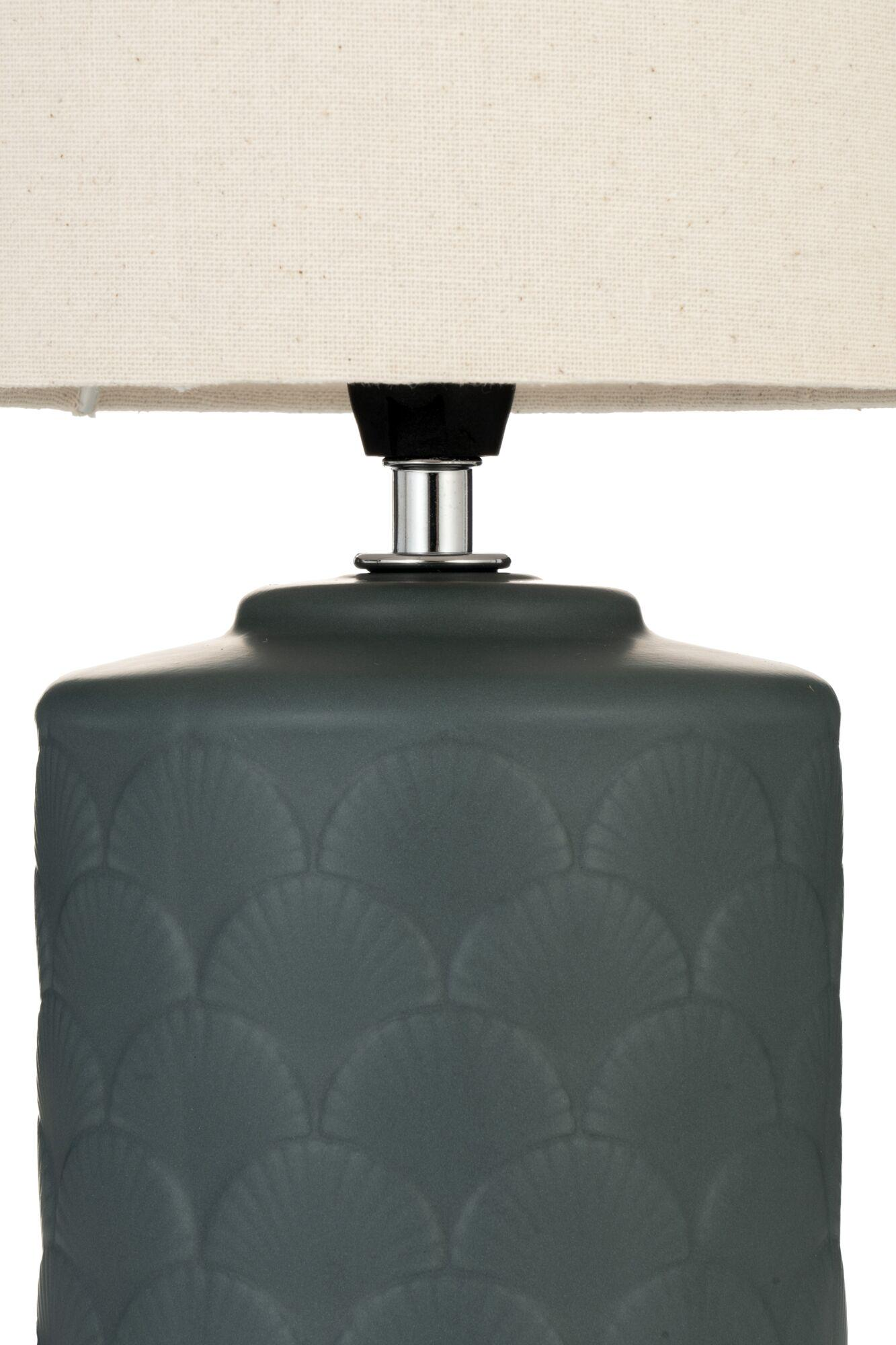 Szara podstawa lampy z białym abażurem. Podstawa ma wzór muszli.