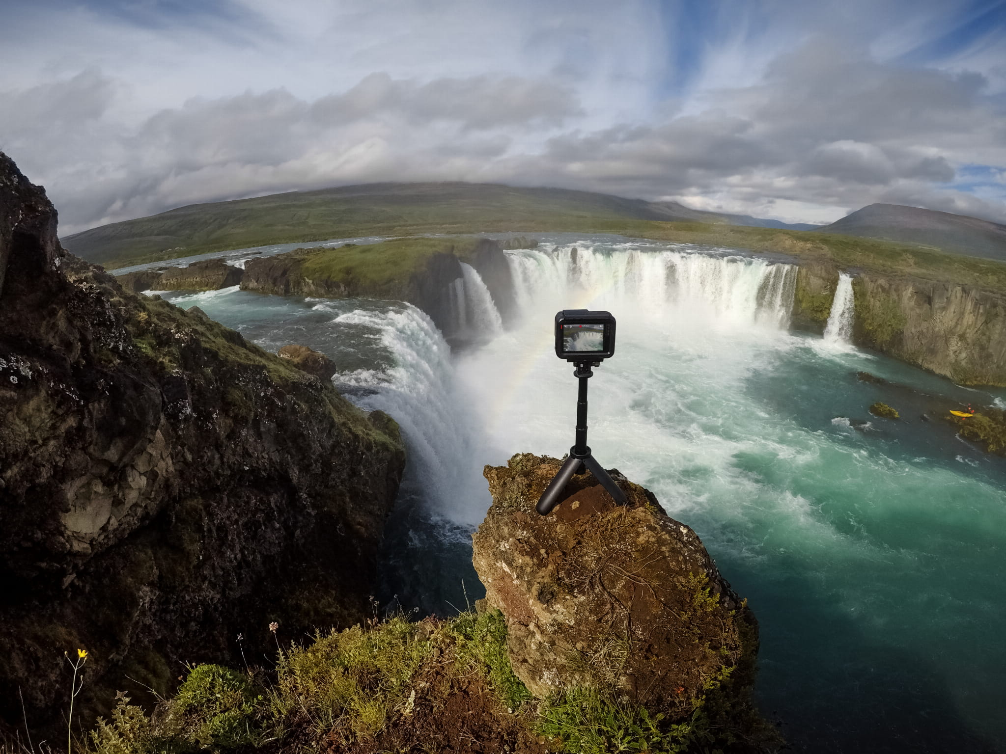 Una cámara en un trípode está configurada para capturar una cascada. El paisaje es verde y azul.