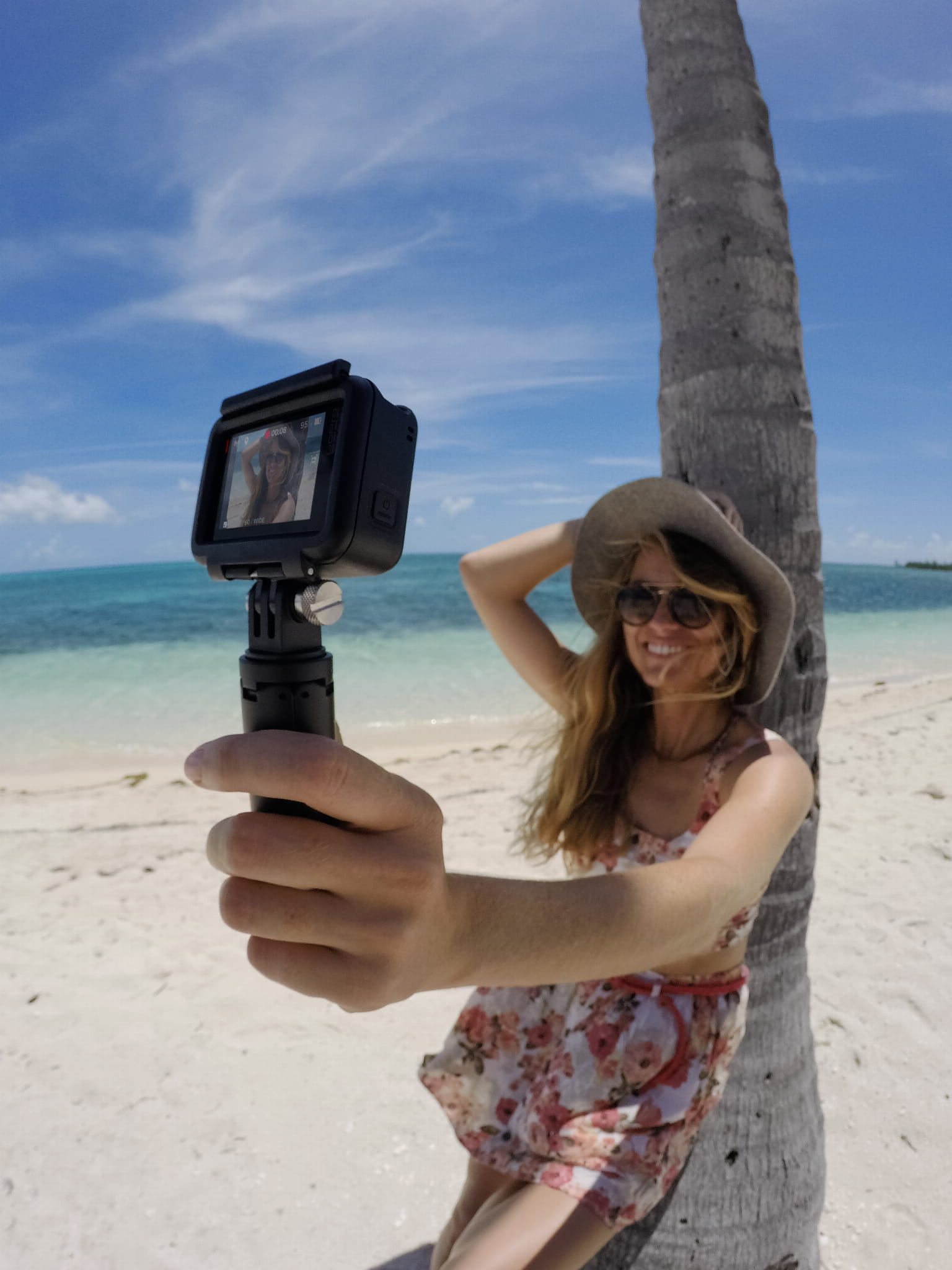 Kobieta robi sobie selfie kamerą na patyku na plaży. Niebieskie niebo i ocean w tle.