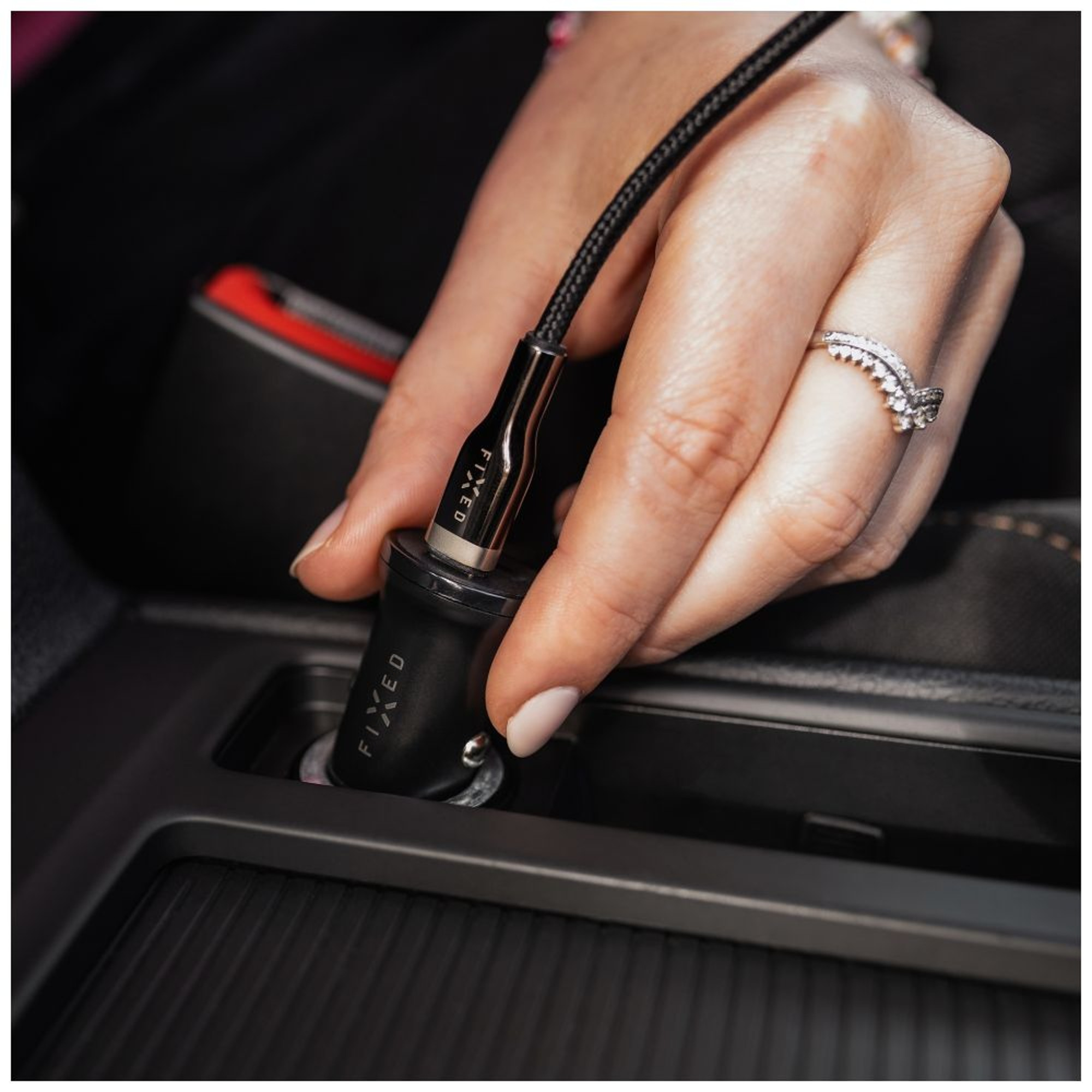 Eine Hand, die ein schwarzes FIXED-Autoladegerät in den Zigarettenanzünder eines Autos steckt. Ein Ring ist sichtbar.