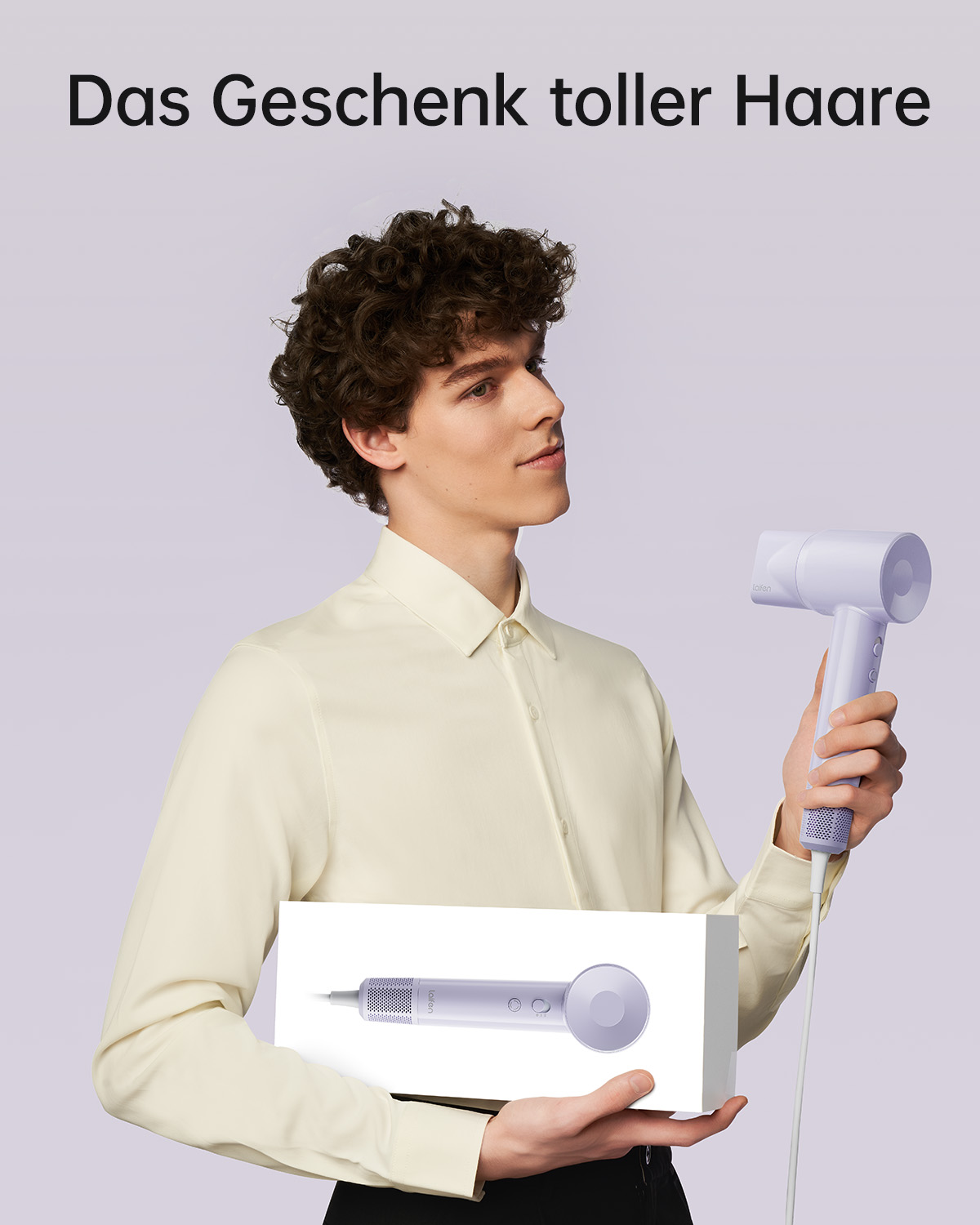 Ein Mann in einem cremefarbenen Hemd hält in einer Studioumgebung eine weiße Schachtel und einen hellvioletten Haartrockner.