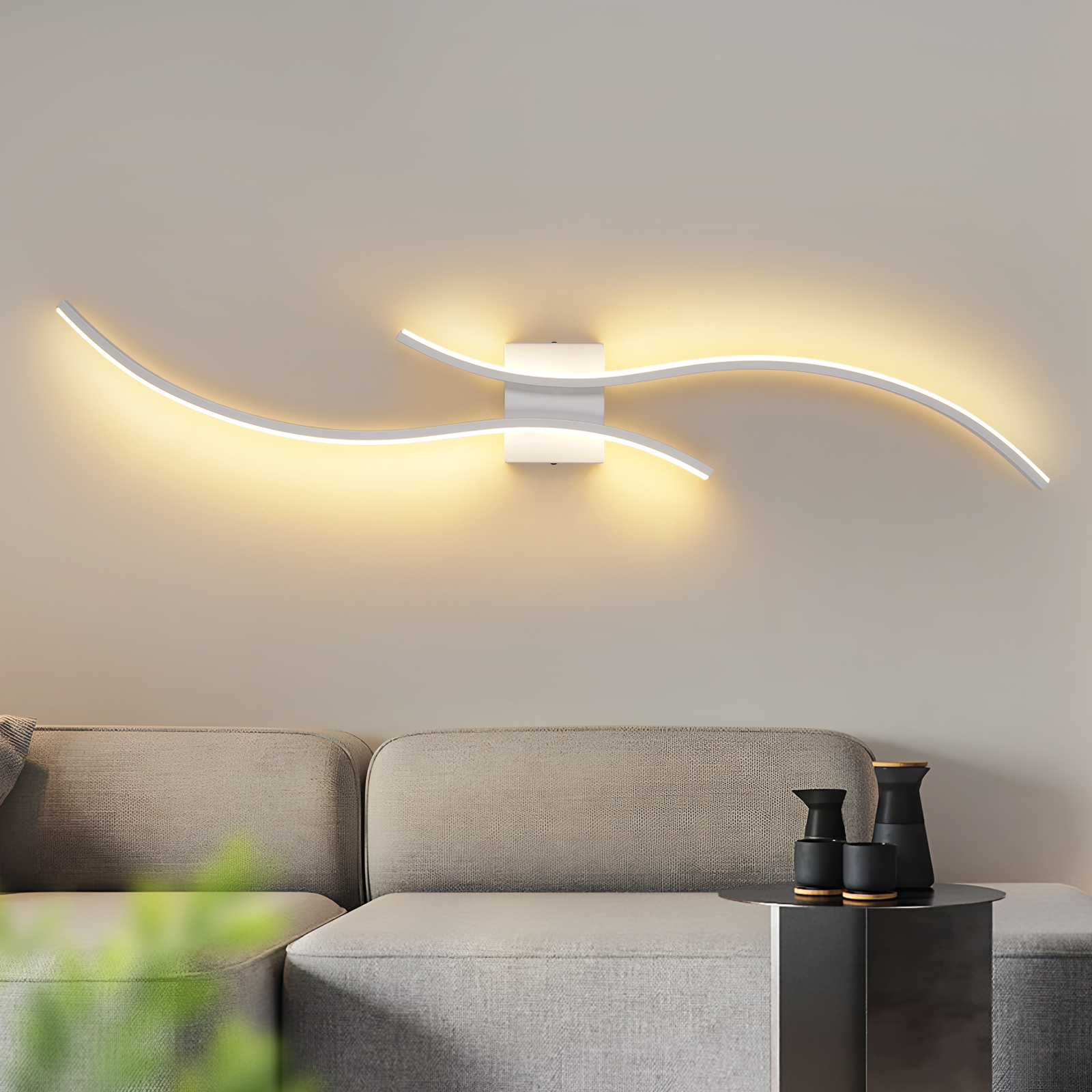 Biała, falista lampa ścienna świeci na beżowej ścianie. Jest szara sofa i stolik z czarnymi wazonami.