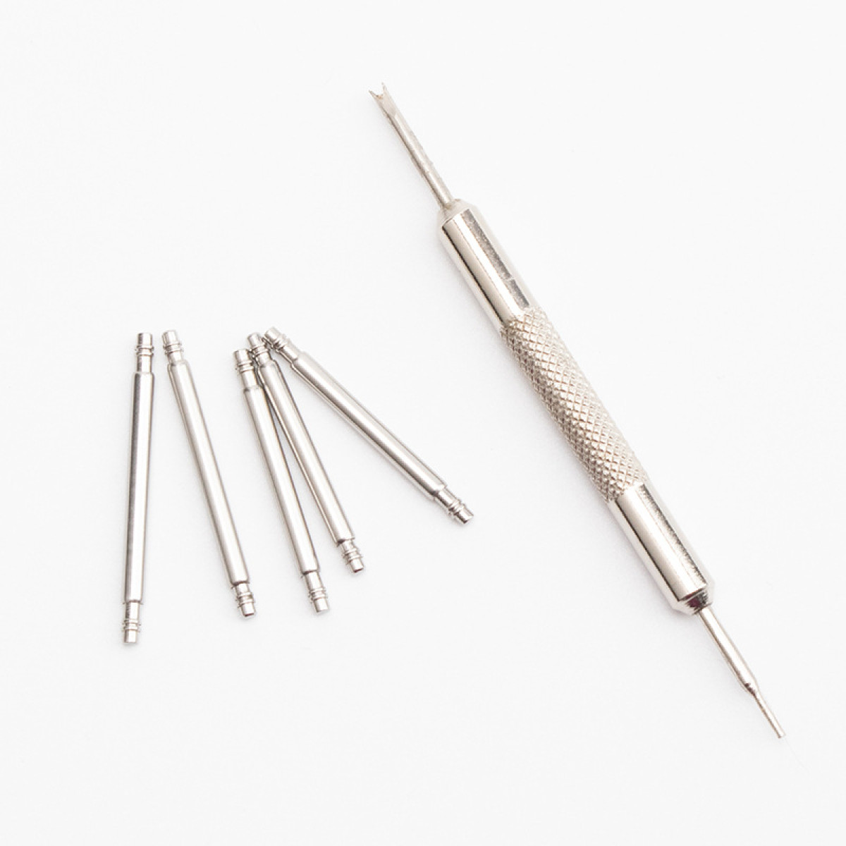 Kilka srebrnych prętów sprężynowych do zegarków i narzędzie na białej powierzchni, prawdopodobnie do regulacji paska.