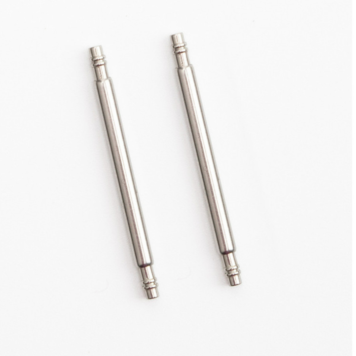 Dwa srebrne szpilki do zegarka o zaokrąglonych końcach, na białym tle.