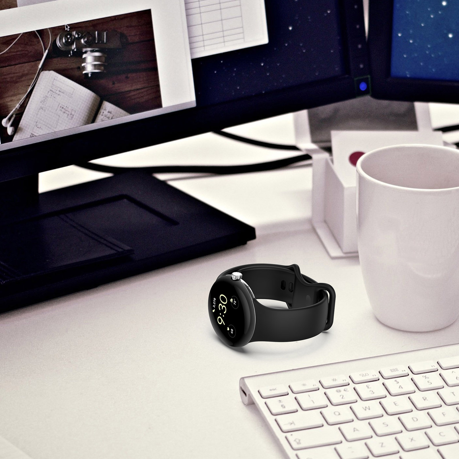 Eine schwarze Smartwatch zeigt 9:30 Uhr auf einem Schreibtisch mit Tastatur, Monitor und weißem Becher.