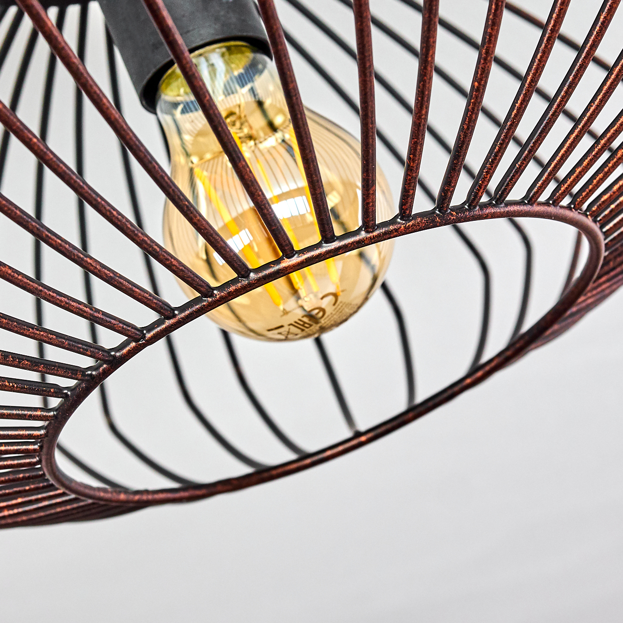Nahaufnahme der Glühbirne einer Deckenlampe. Die Lampe hat eine kupferne Farbe und ein Drahtrahmen-Design.