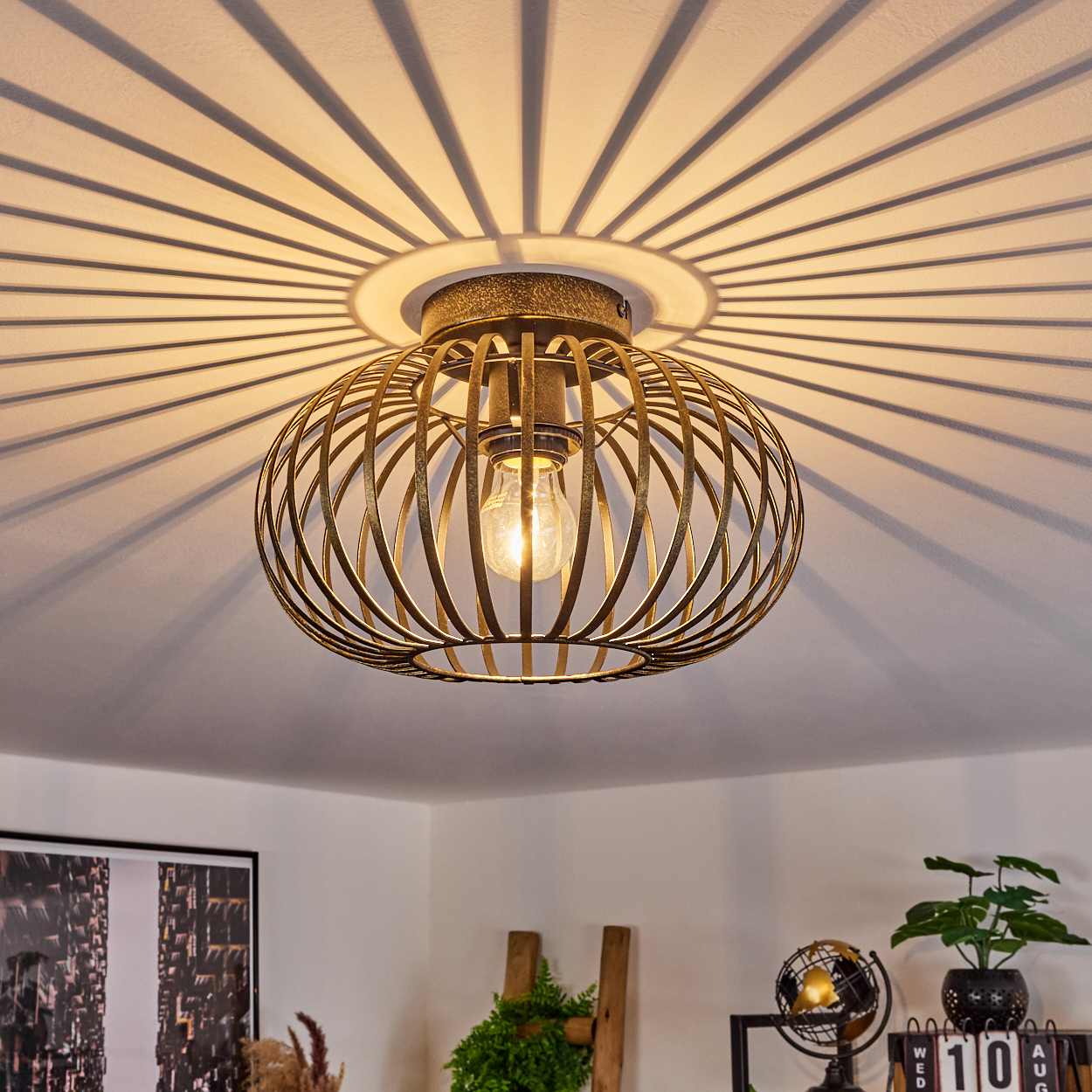 Deckenleuchte mit goldenem käfigartigem Design. Sie wirft ein radiales Schattenmuster an die Decke.