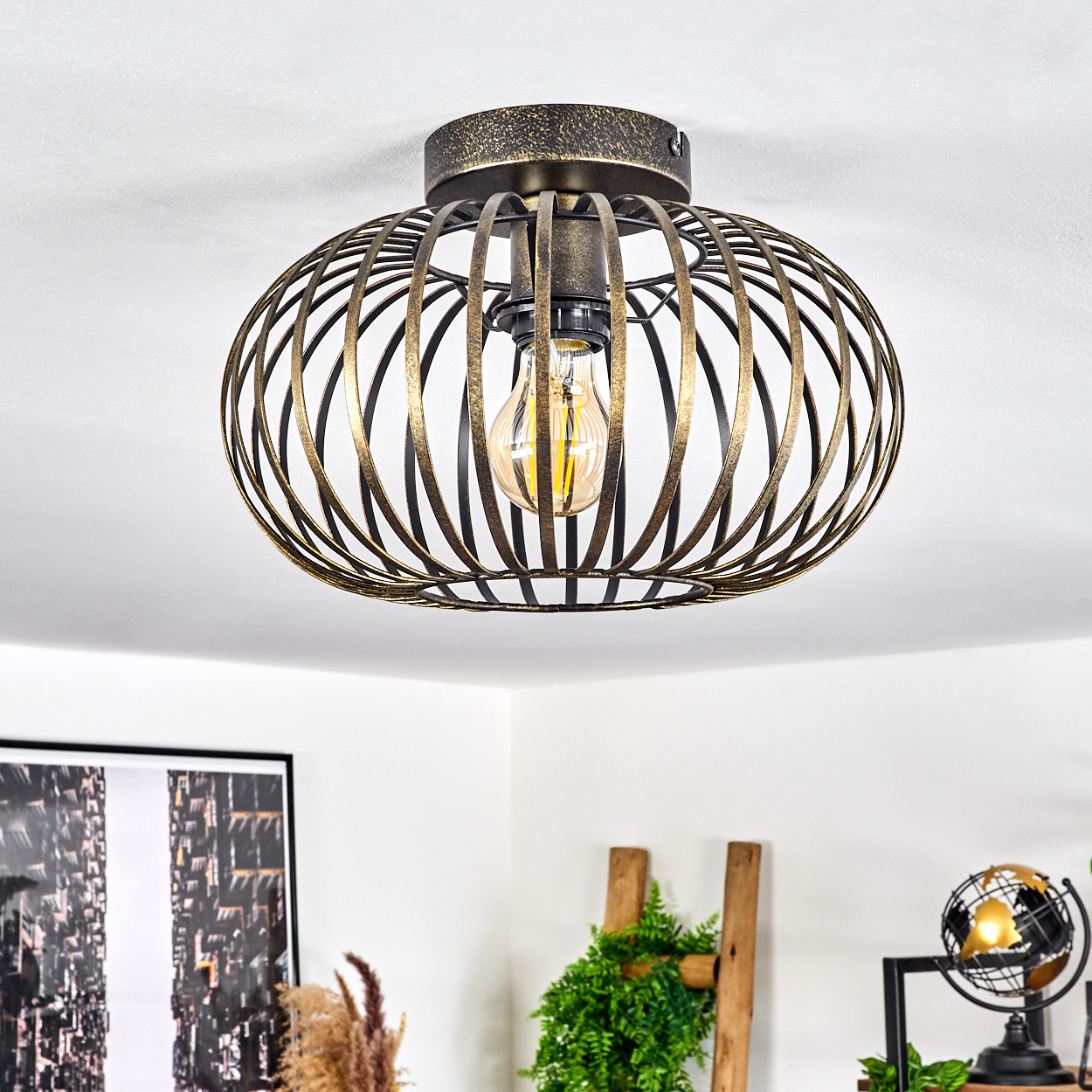 Ovale, käfigartige Deckenlampe mit sichtbarer Glühbirne. Die Lampe ist gold und dunkel.