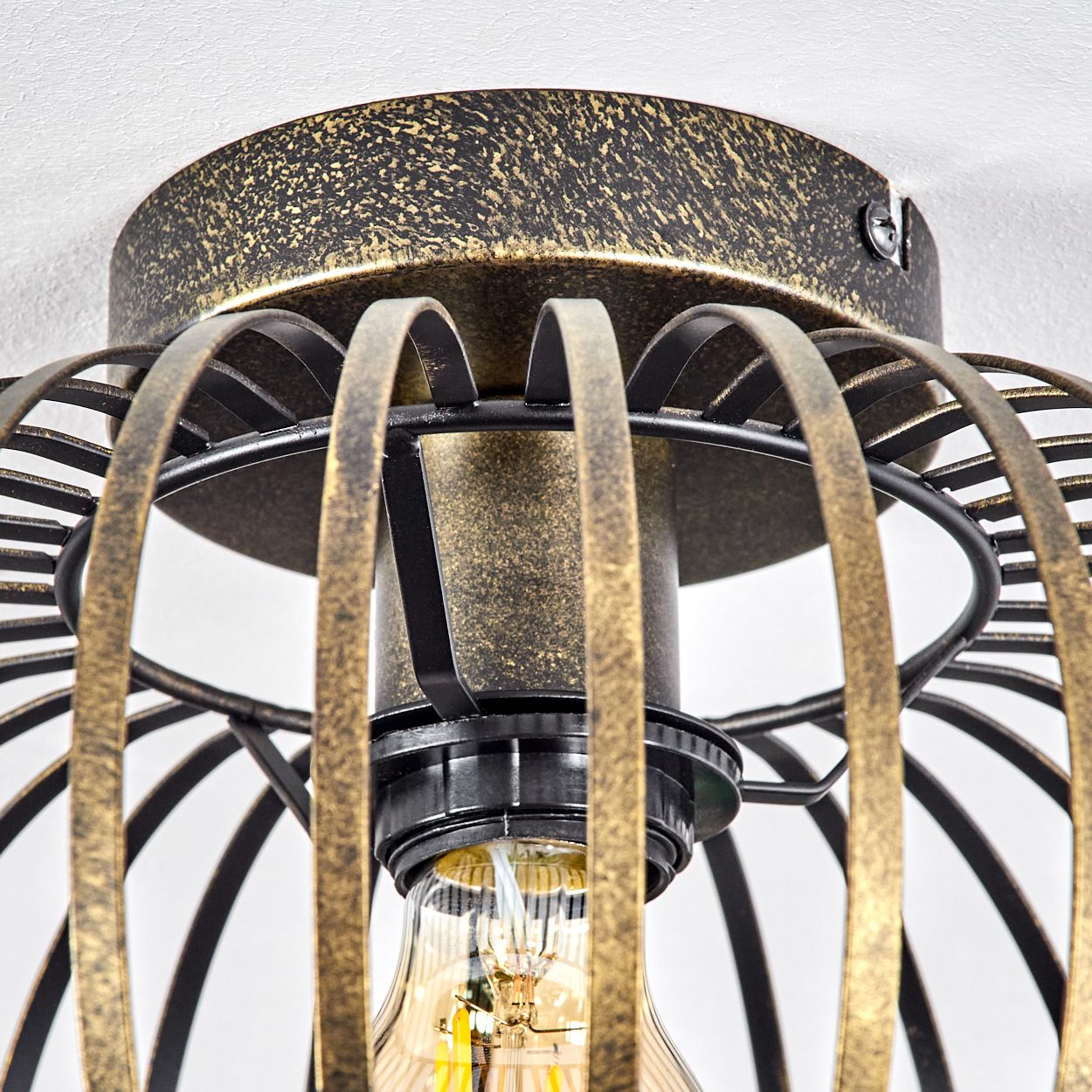 Nahaufnahme einer Deckenlampe mit Käfigdesign. Die Lampe hat eine goldene und dunkle Metalloberfläche.