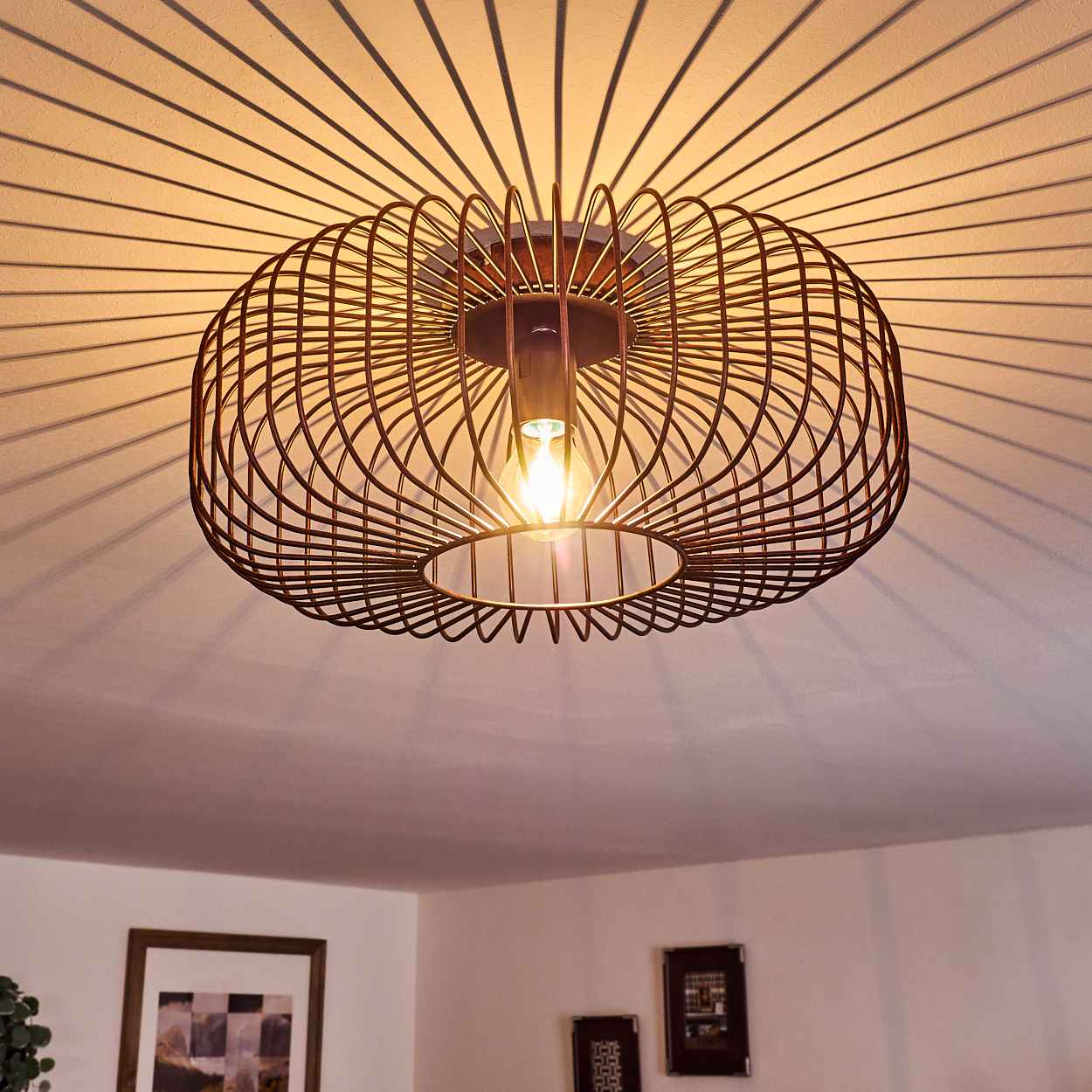 Deckenleuchte mit Käfigdesign, das Lichtmuster auf die weiße Decke wirft.