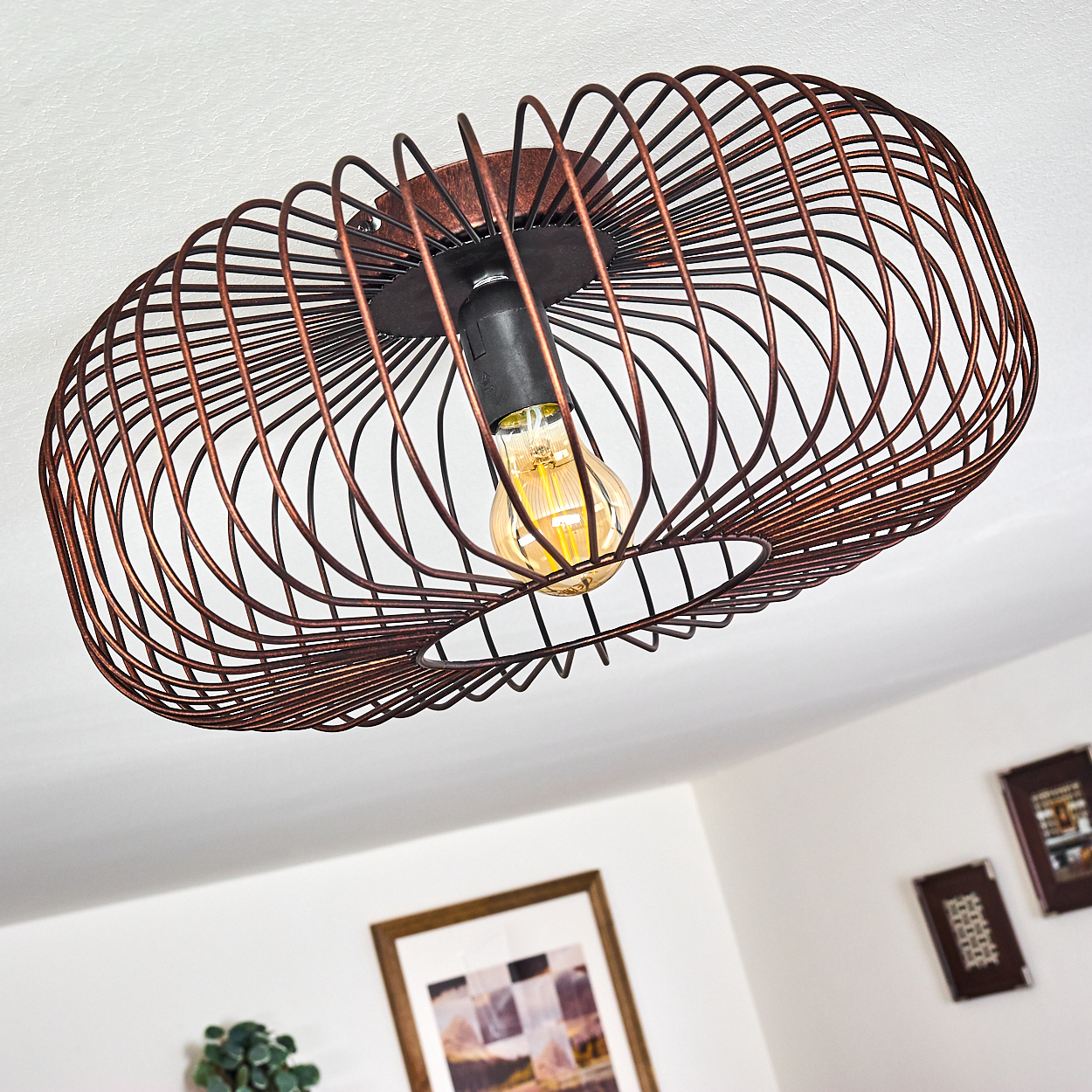 Deckenleuchte mit Käfigdesign, wirft Licht auf die Decke. Die Glühbirne ist sichtbar.