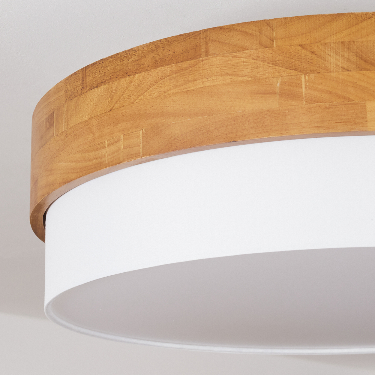 Nahaufnahme einer holzverkleideten Deckenlampe mit weißem Schirm. Das Holz hat einen geschichteten Look.