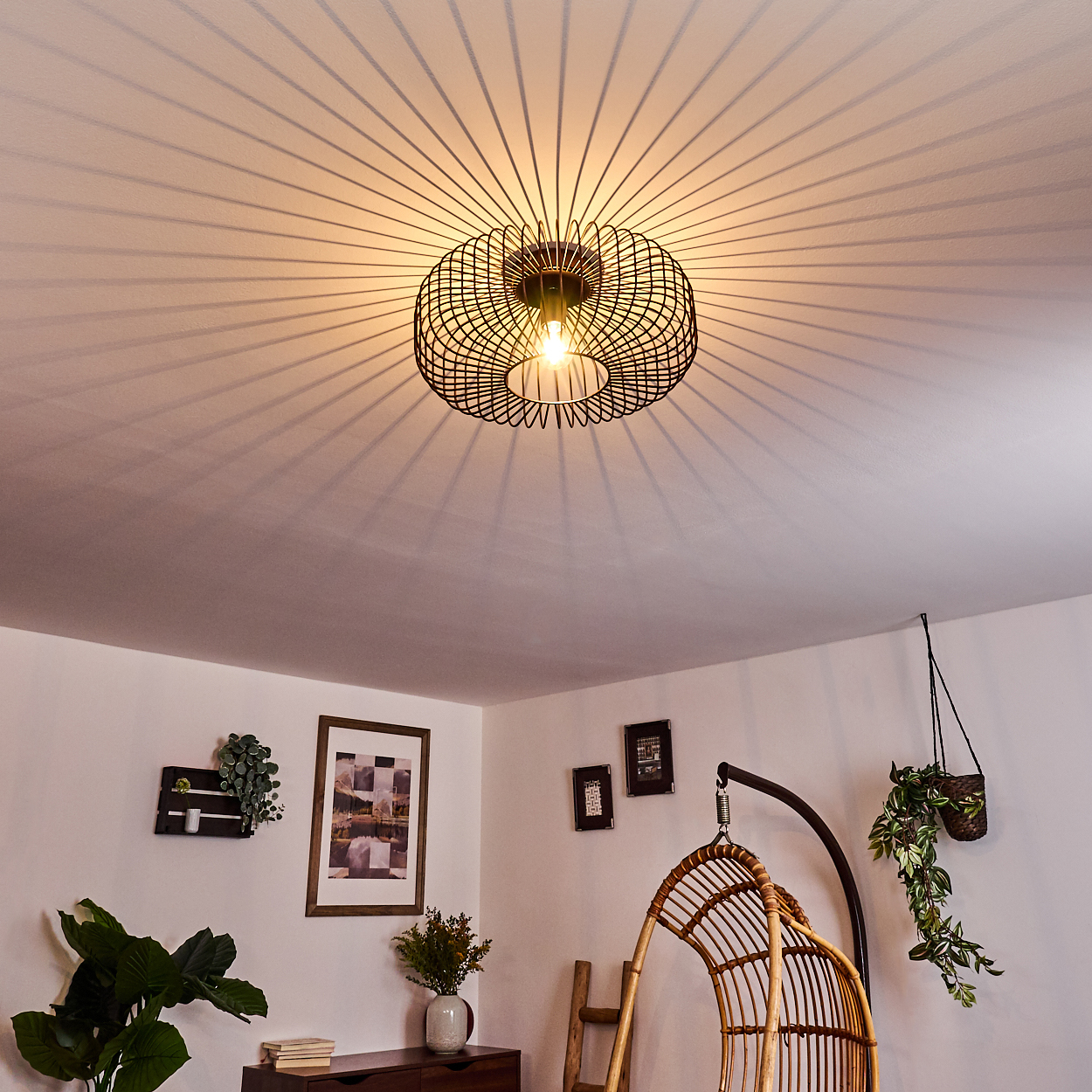 Deckenleuchte mit Drahtrahmen, wirft lineare Schatten an die Decke.