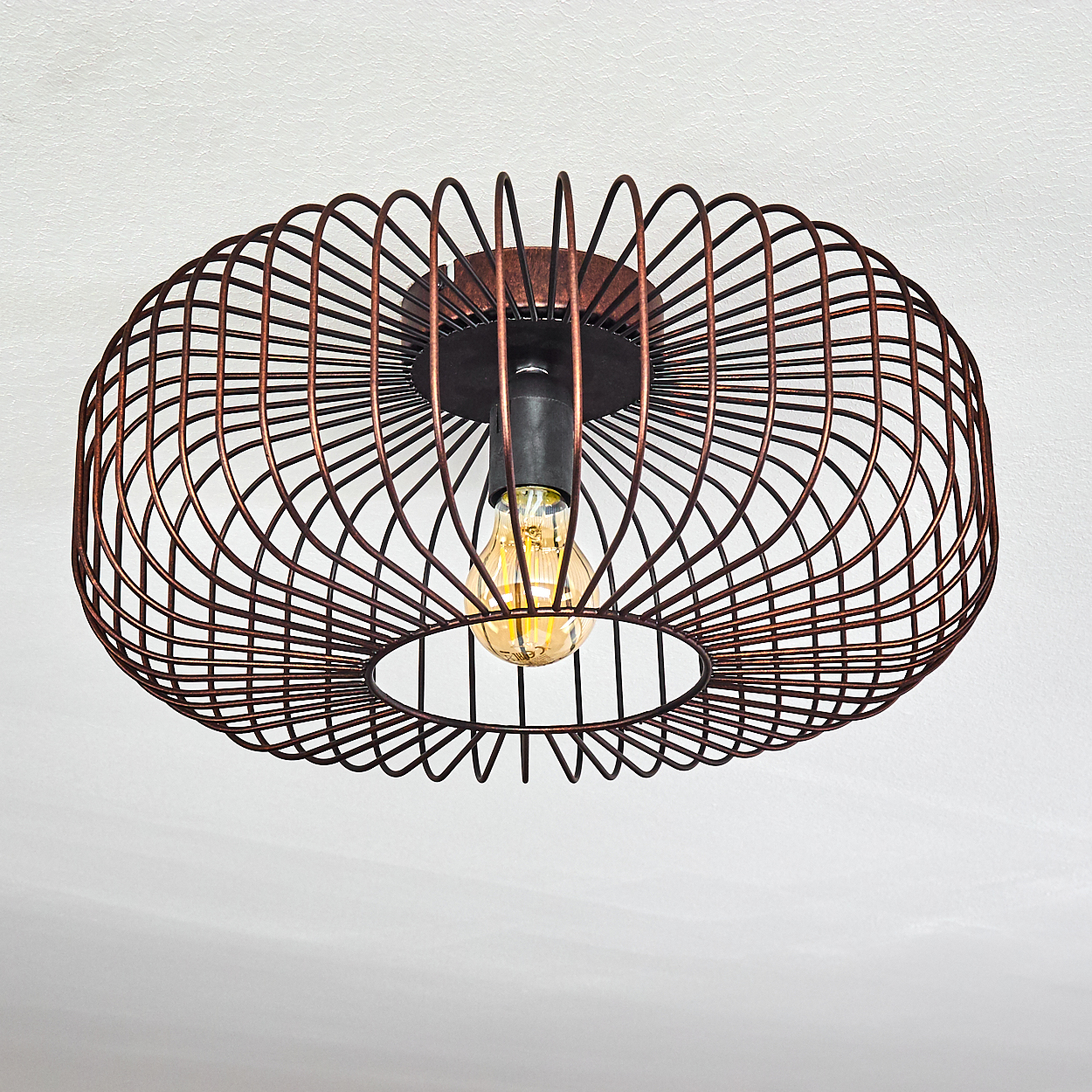 Kupferfarbene Metall-Drahtkäfig-Deckenlampe mit sichtbarer Glühbirne. Der Hintergrund ist eine weiße Decke.