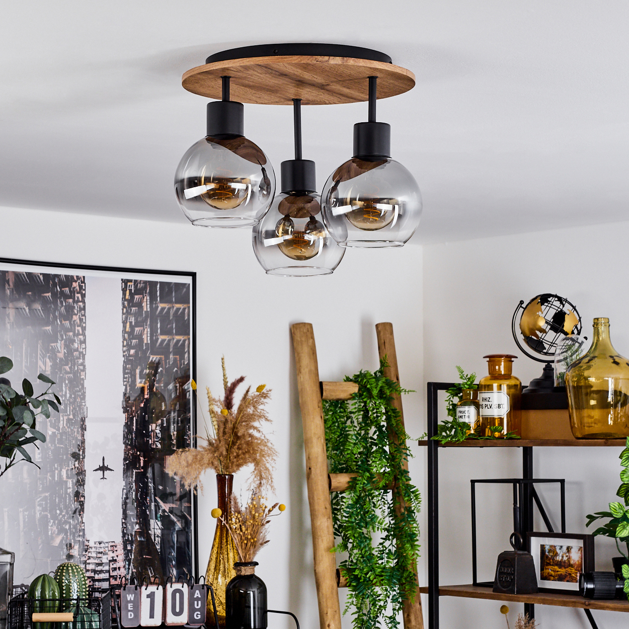 Deckenlampe mit drei Glasschirmen, Holzsockel und Dekoration in einem Raum. Die Lampe ist der Fokus.