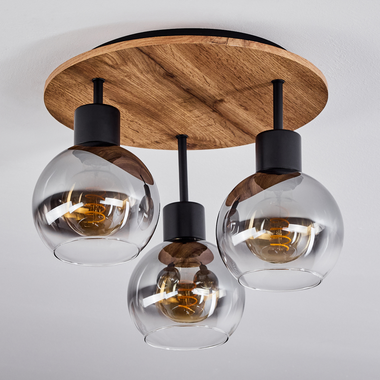 Deckenlampe mit drei Glaskugel-Schirmen, Holzsockel. Die Lampe ist der Fokus vor weißer Decke.