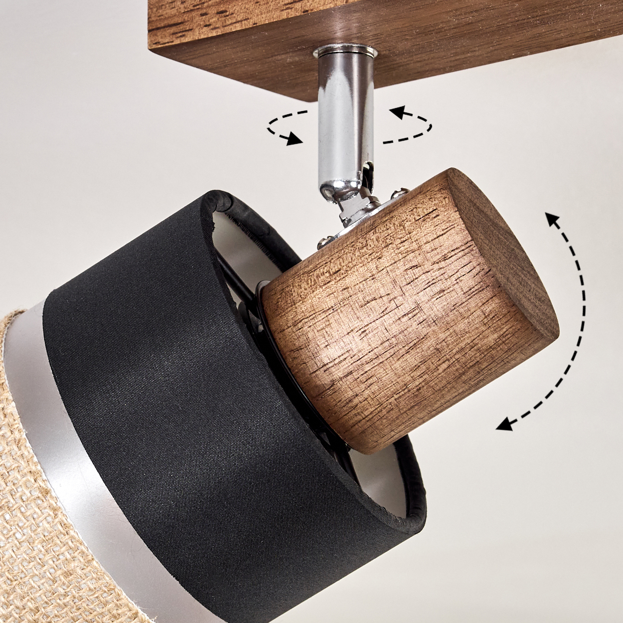 Ein Strahler mit schwarzem Schirm und beigem Gewebe, an einer Holzbasis befestigt. Pfeile zeigen die Drehung an.