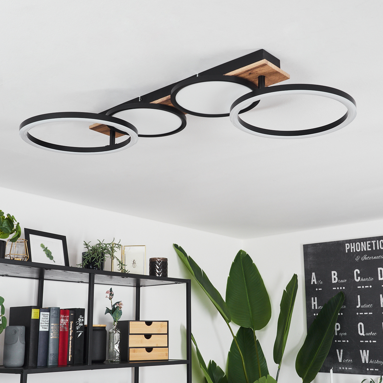 Eine Deckenlampe mit vier schwarzen Ringen mit weißem Licht und Holzelementen wird gezeigt.