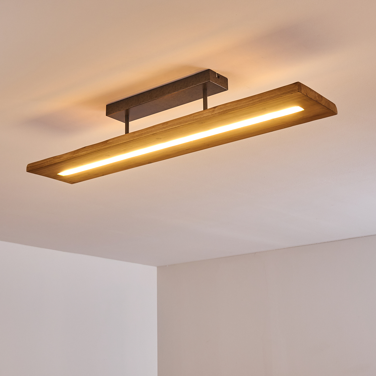 Rechteckige Deckenleuchte aus Holz mit hellem Lichtstreifen in der Mitte, an einer weißen Decke befestigt.