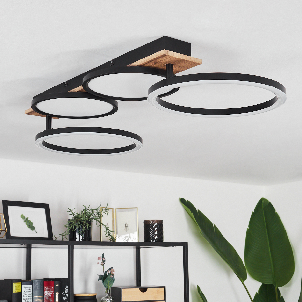 Eine Deckenlampe mit vier schwarzen Ringen mit weißem Licht und Holzelementen, die eine Raumeinstellung zeigt.