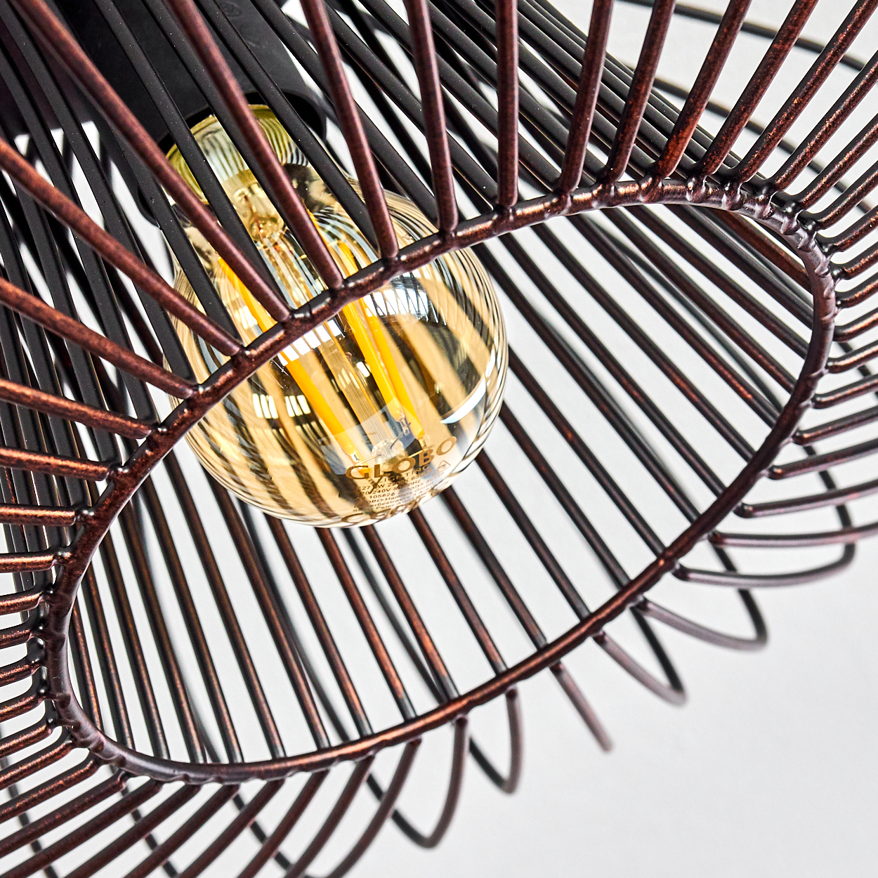 Nahaufnahme einer Glühbirne in einer Drahtrahmen-Deckenlampe. Die Glühbirne leuchtet und der Rahmen ist metallisch.