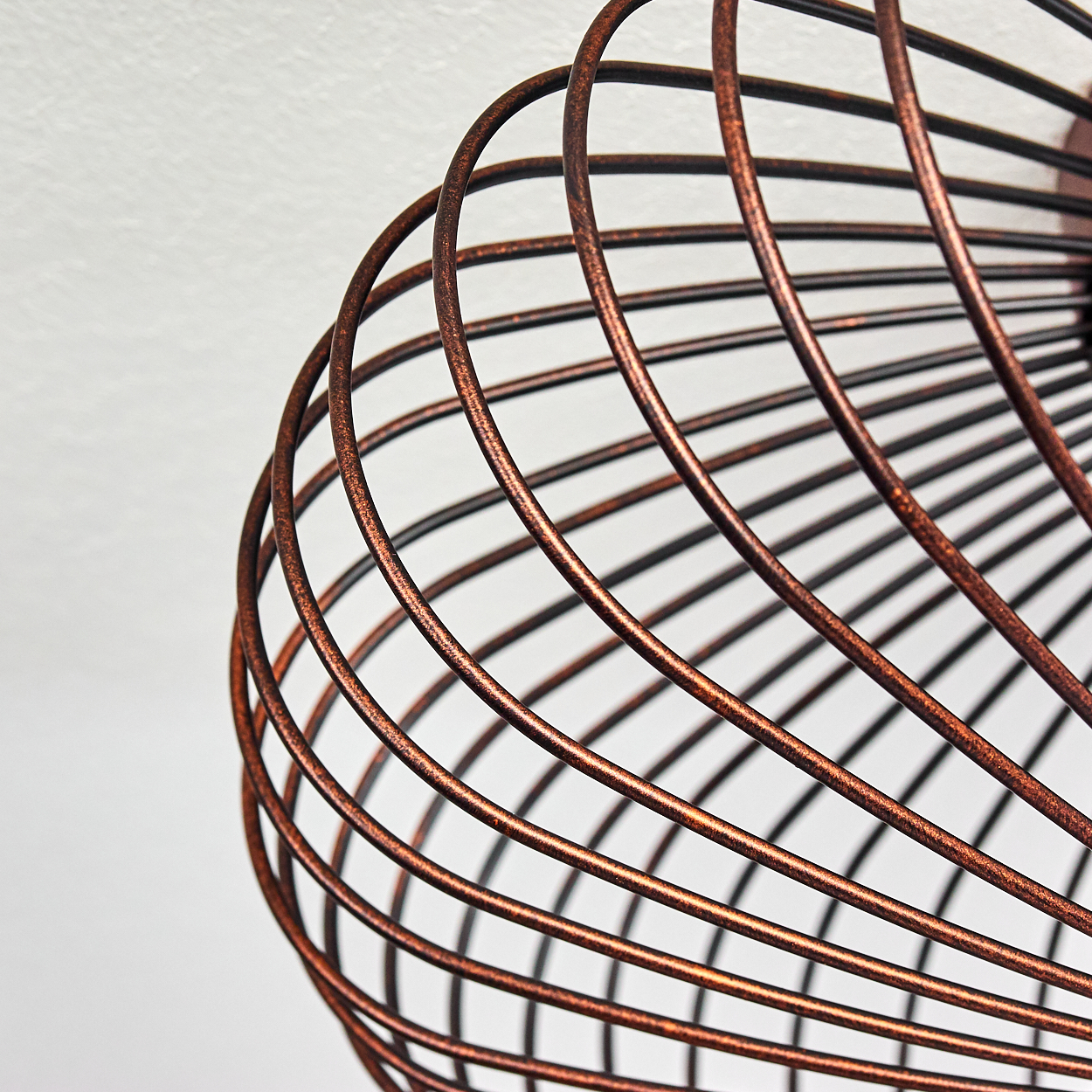 Nahaufnahme des kupferfarbenen Drahtrahmens einer Deckenlampe, die ihre geschwungenen Linien zeigt.