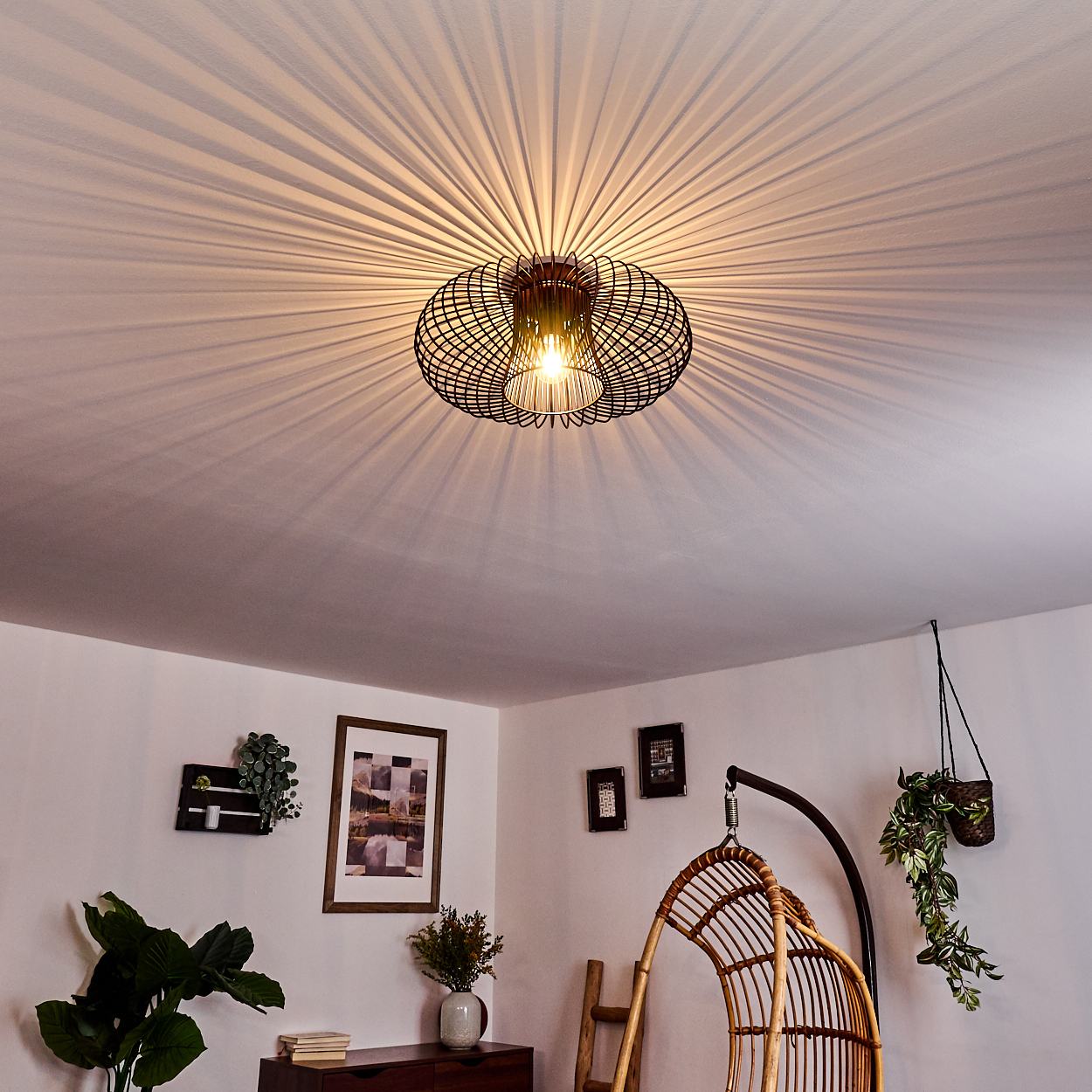 Innenraum mit einer Drahtrahmen-Deckenlampe und anderen Dekoelementen wie einer Schaukel und gerahmten Bildern.