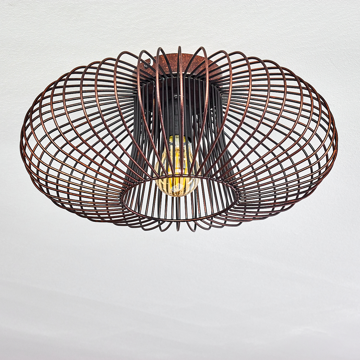 Die Drahtrahmenlampe befindet sich an einer Decke. Der Rahmen ist kupferfarben. Das Licht ist an.
