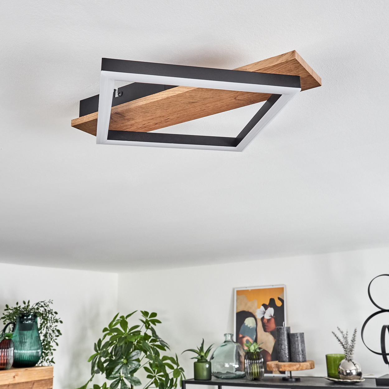 Eine Deckenlampe mit Holz- und schwarzem Rahmen, weißem Innenlicht und einem Holzregal. Pflanzen im Vordergrund.