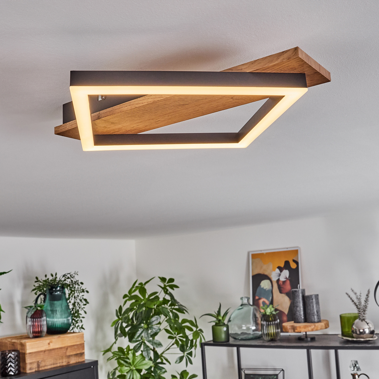 Eine Deckenlampe mit Holz- und schwarzem Rahmen, weißem Innenlicht. Pflanzen und Deko im Vordergrund.