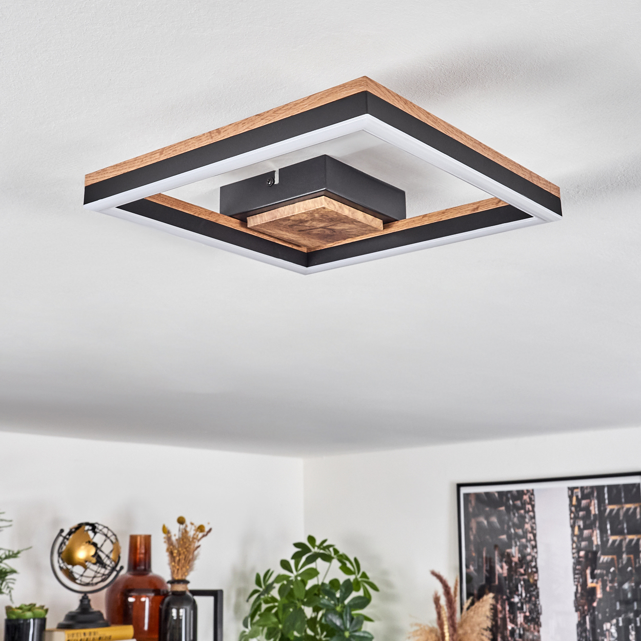 Deckenleuchte mit Holz- und schwarzen quadratischen Rahmen, die Licht aussendet. Vor einer weißen Decke.