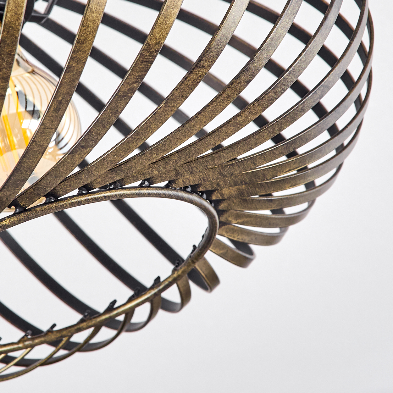 Nahaufnahme des spiralförmigen Drahtrahmens einer Lampe. Eine Glühbirne ist im Rahmen sichtbar. Weißer Hintergrund.