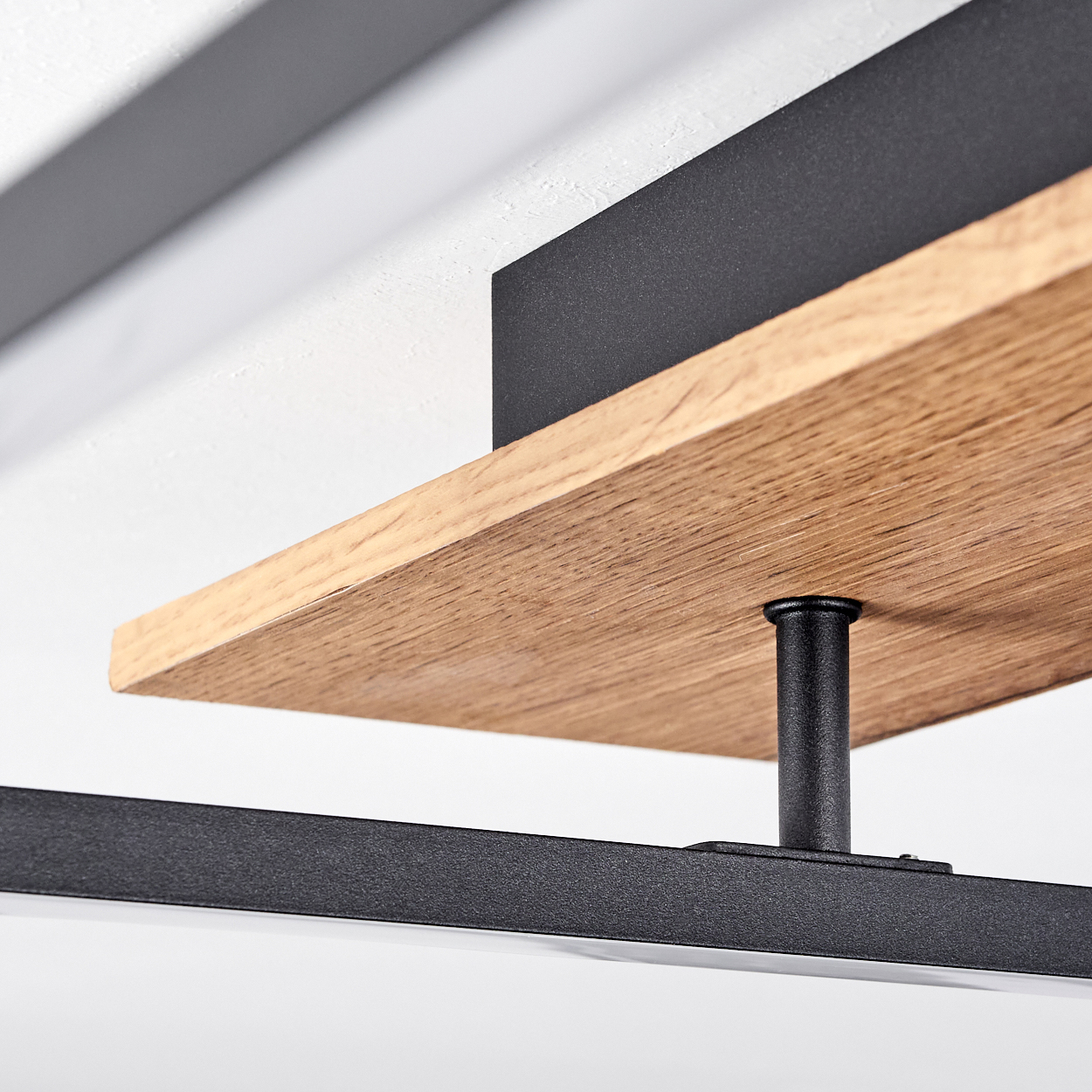 Nahaufnahme: Holzplanke und schwarzer Rahmen einer Deckenlampe. Weißer Lichtstreifen ist sichtbar. Weiße Decke.