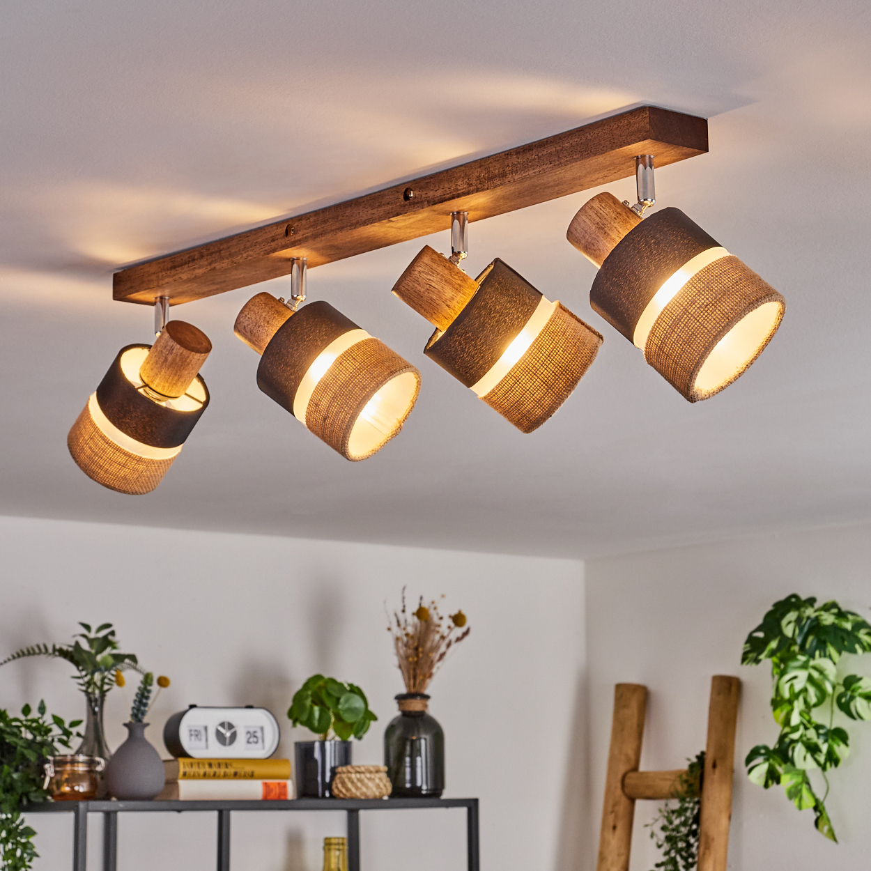Eine Decke mit einem Holzbalken und vier Strahlern. Die Lampen sind abgewinkelt, und ein warmes Licht scheint aus ihnen.