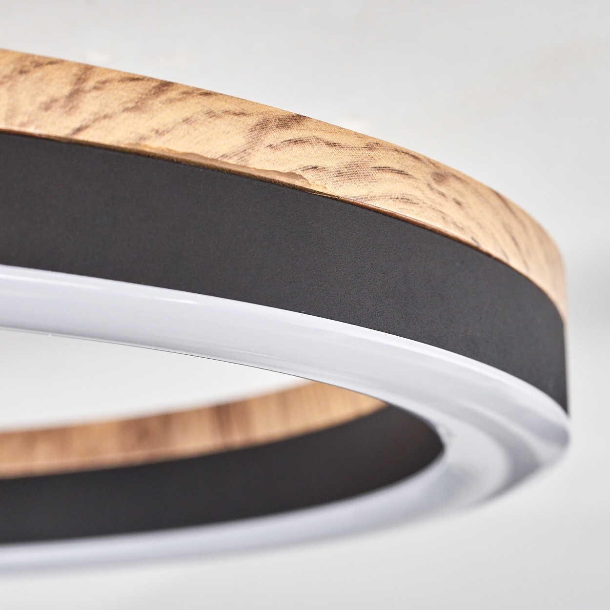 Nahaufnahme einer Deckenleuchte. Holz- und schwarzer Ring mit weißem Lichtband. Weißer Hintergrund.