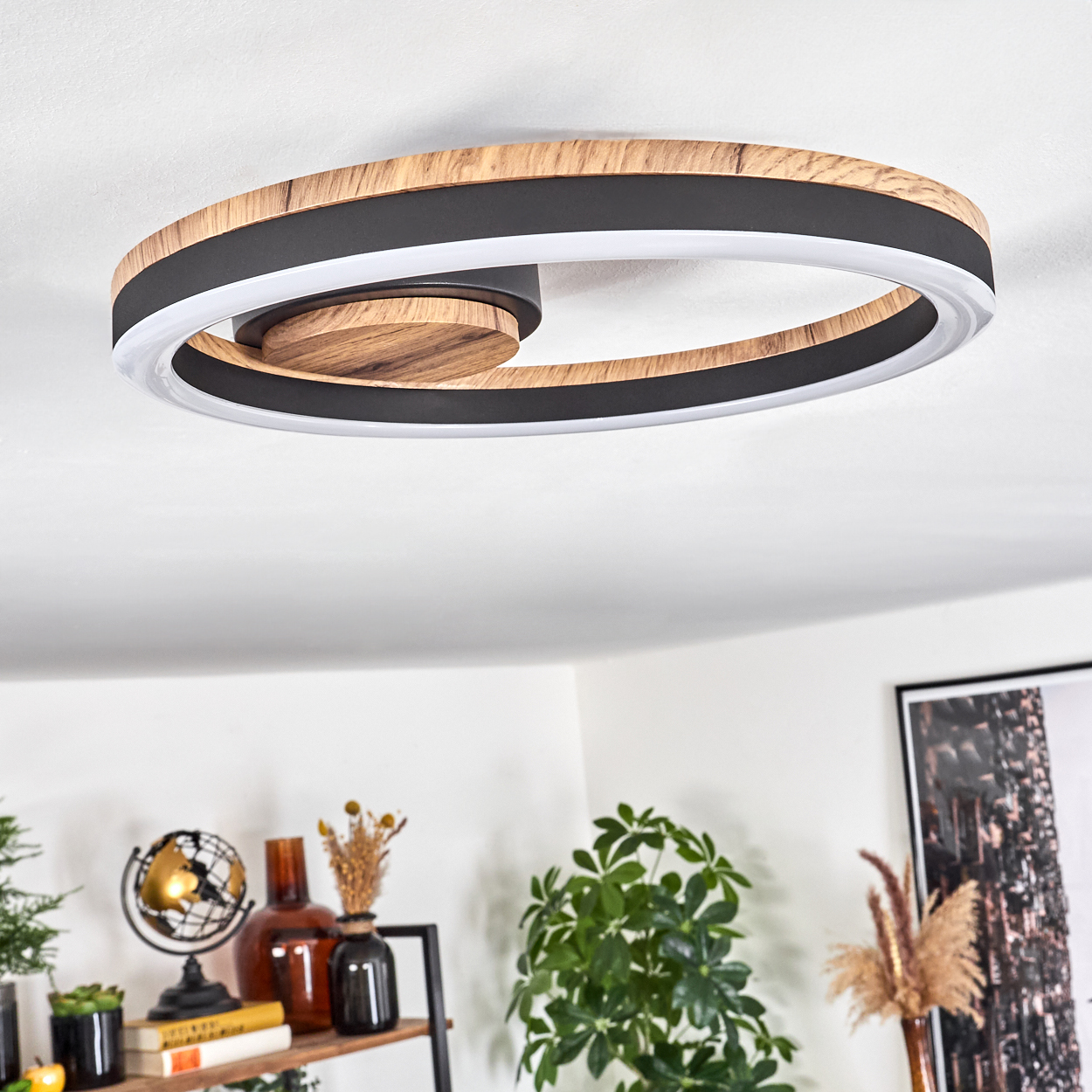 Kreisförmige Deckenleuchte mit Holzmitte, schwarzem Ring und weißem Licht. Im Hintergrund Dekoration und eine Pflanze.