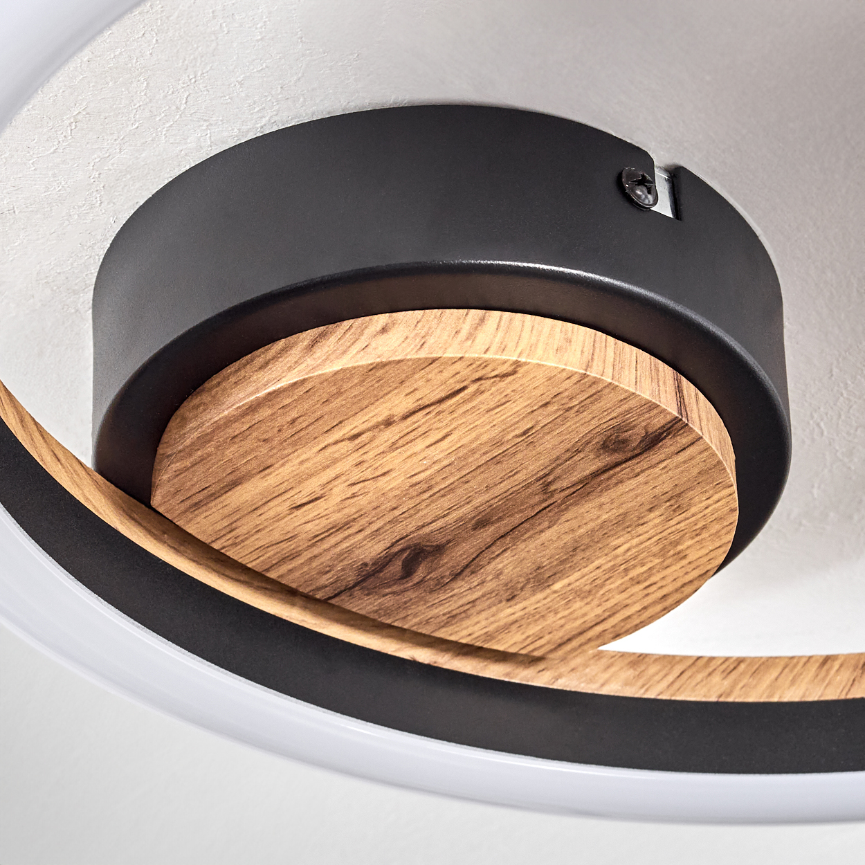Nahaufnahme einer Deckenleuchte mit Holz- und Schwarzelementen. Die Leuchte hat eine kreisförmige Holzbasis und einen schwarzen Ring.
