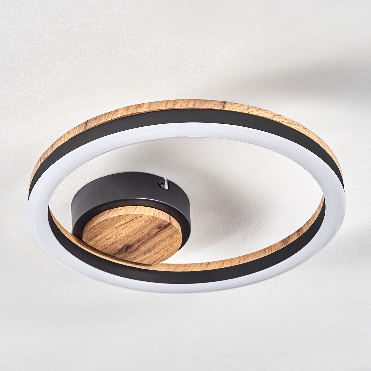 Kreisförmige Deckenleuchte mit Holzmitte, schwarzem Ring und weißem Licht. Der Hintergrund ist weiß.