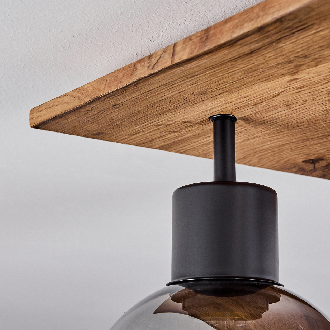 Das Bild zeigt eine Nahaufnahme einer schwarzen Lampenbefestigung, die an einer Holzdeckenplatte befestigt ist.