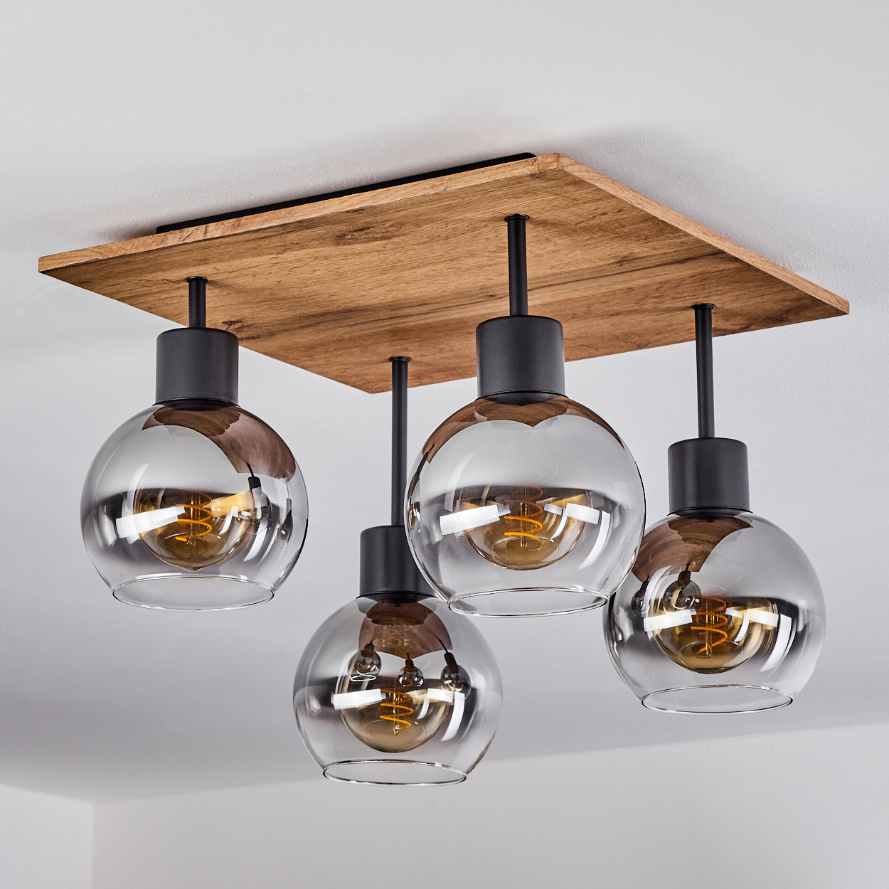 Eine Deckenlampe mit vier Glaskugeln mit sichtbaren Glühbirnen, vor einer weißen Decke.