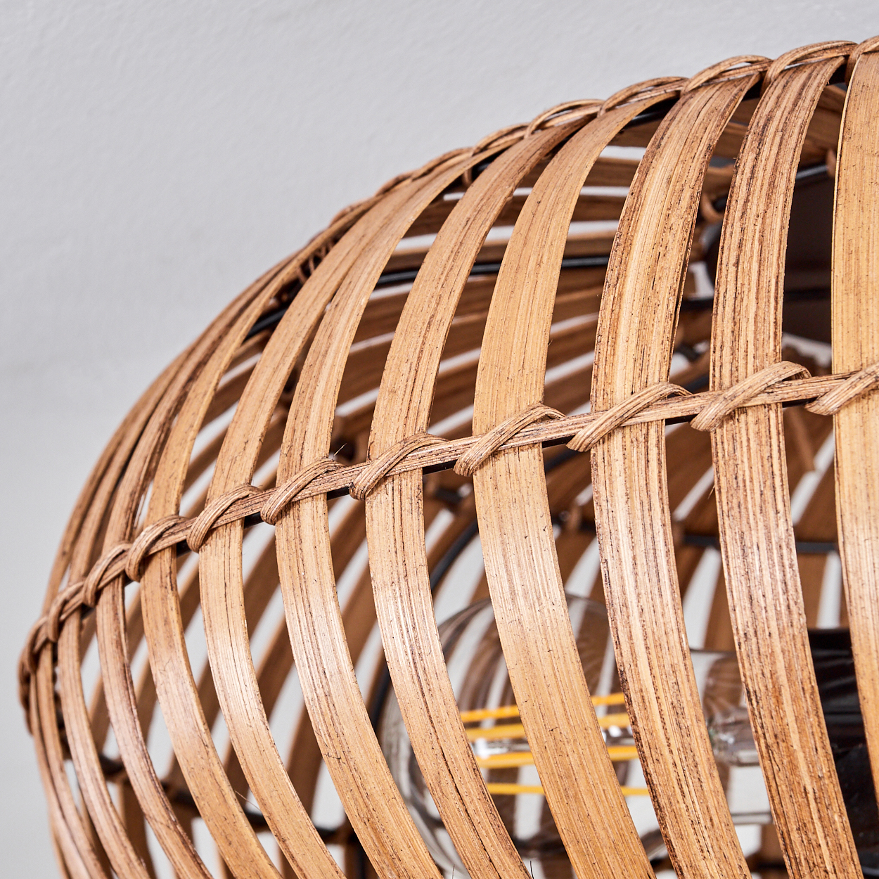 Nahaufnahme der gewebten Textur einer Rattanlampe, hellbraune Farbe und sichtbare Glühbirne.