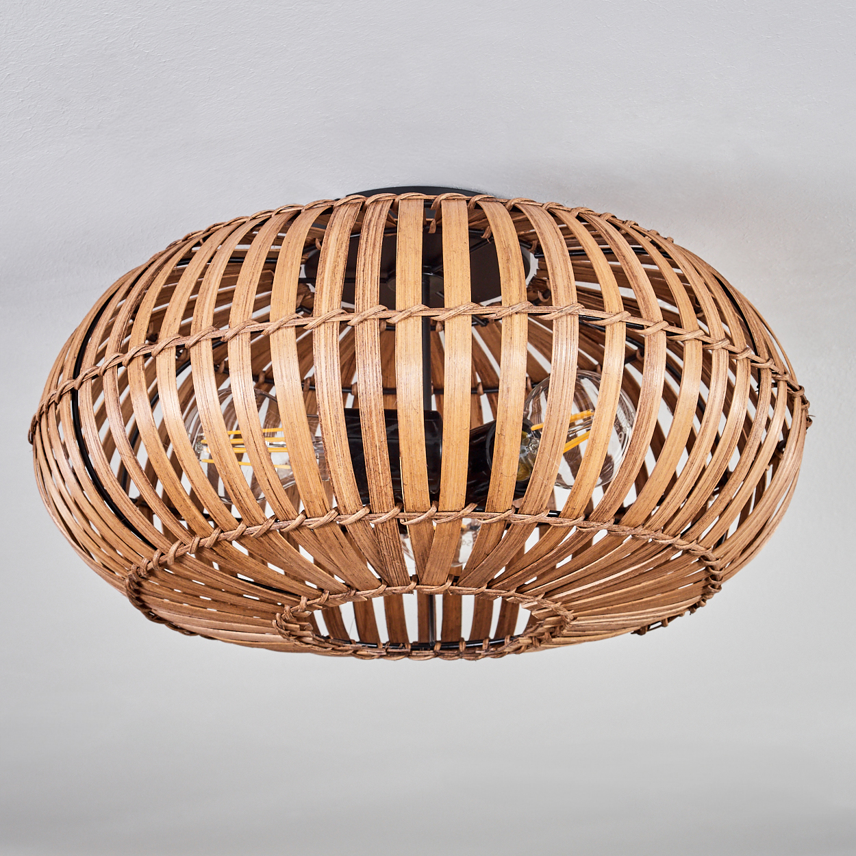 Eine Rattan-Deckenlampe mit Glühbirnen, die Schatten an die Decke wirft.