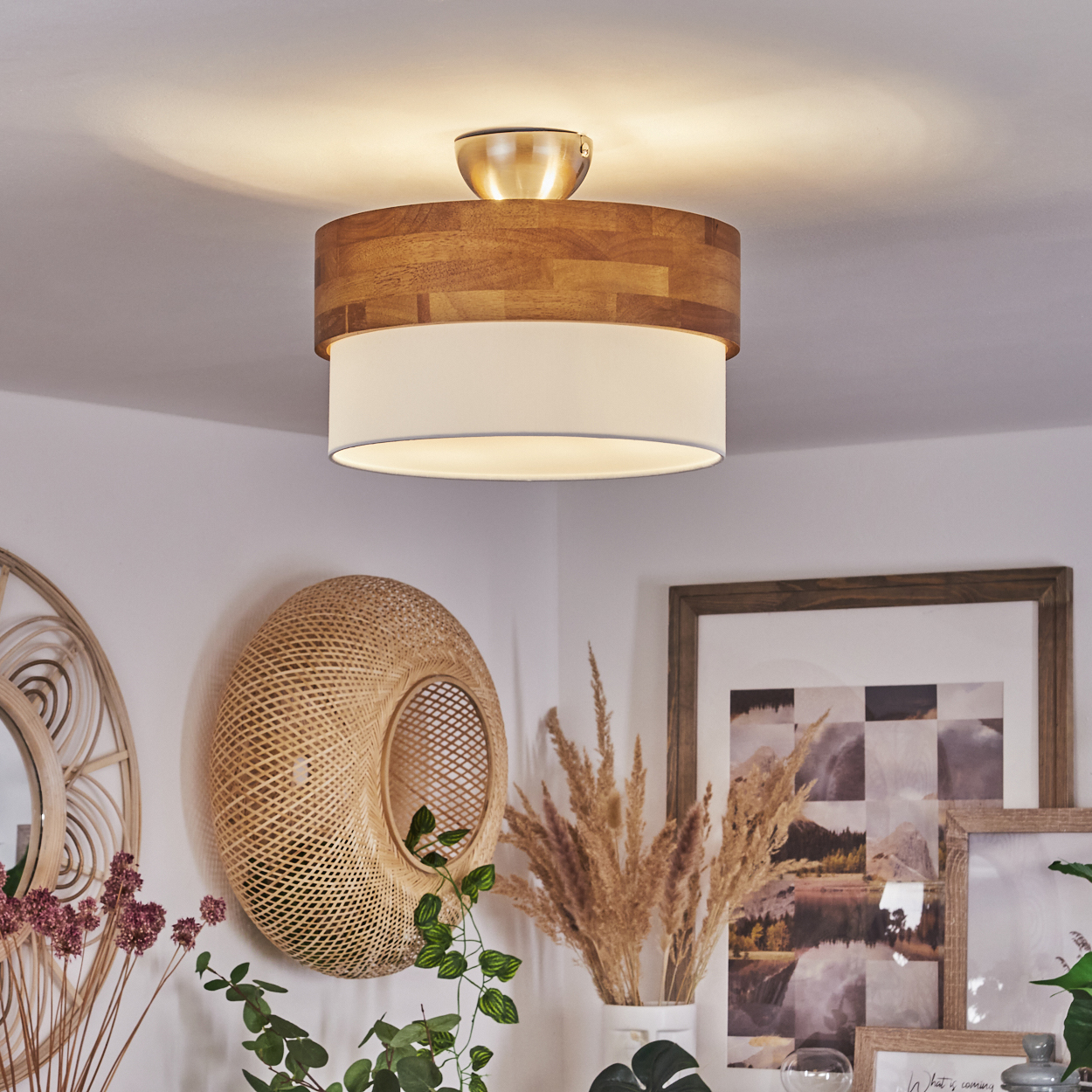 Eine Deckenleuchte mit Holz- und weißem Lampenschirm. Der Hintergrund zeigt eine Wand mit Dekorationen und Pflanzen.