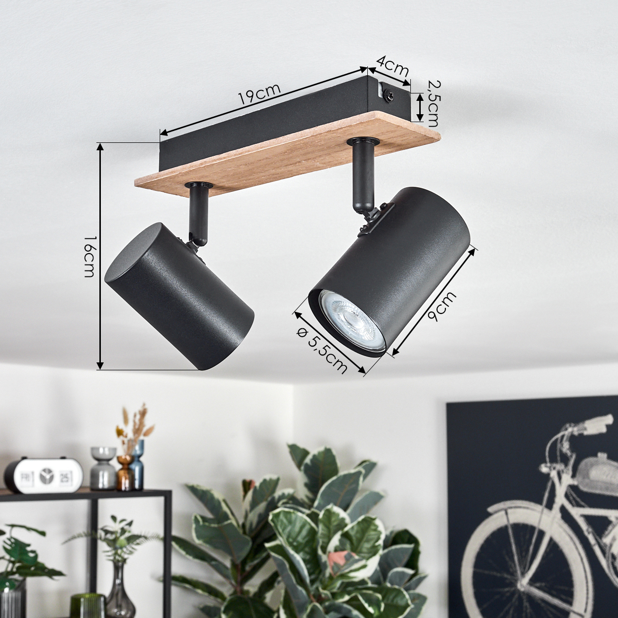 Zwei schwarze Strahler auf einem Holzbrett mit Abmessungen. Die Strahler an einer weißen Decke, mit Fahrradbild.
