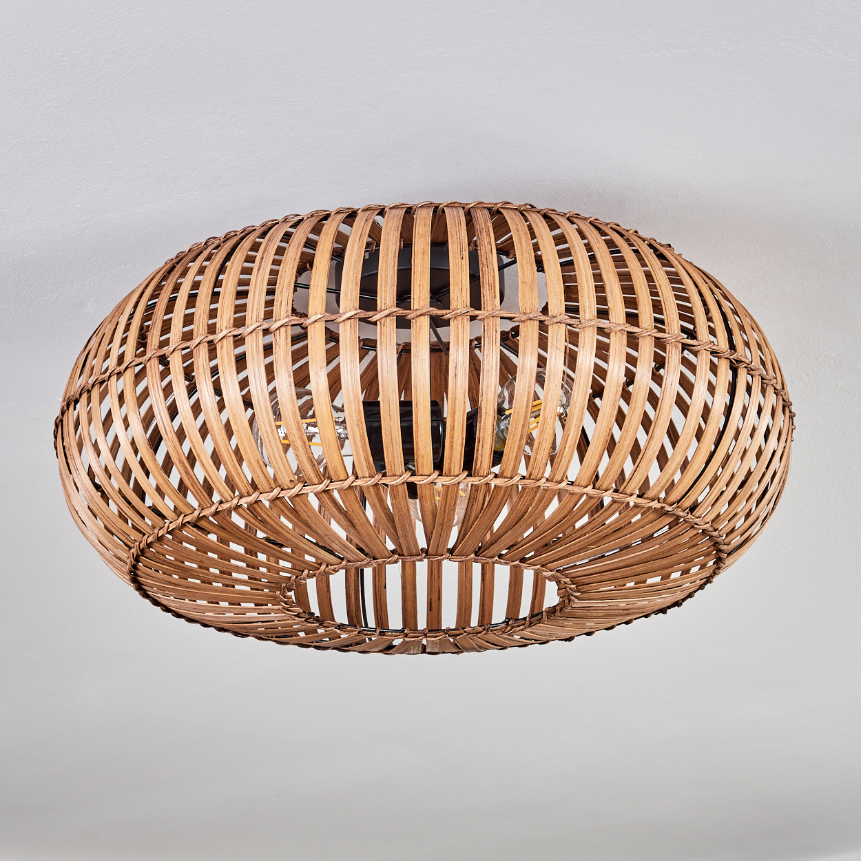Eine Deckenleuchte aus geflochtenem Rattan. Die Lampe ist oval und beleuchtet den Raum warm.